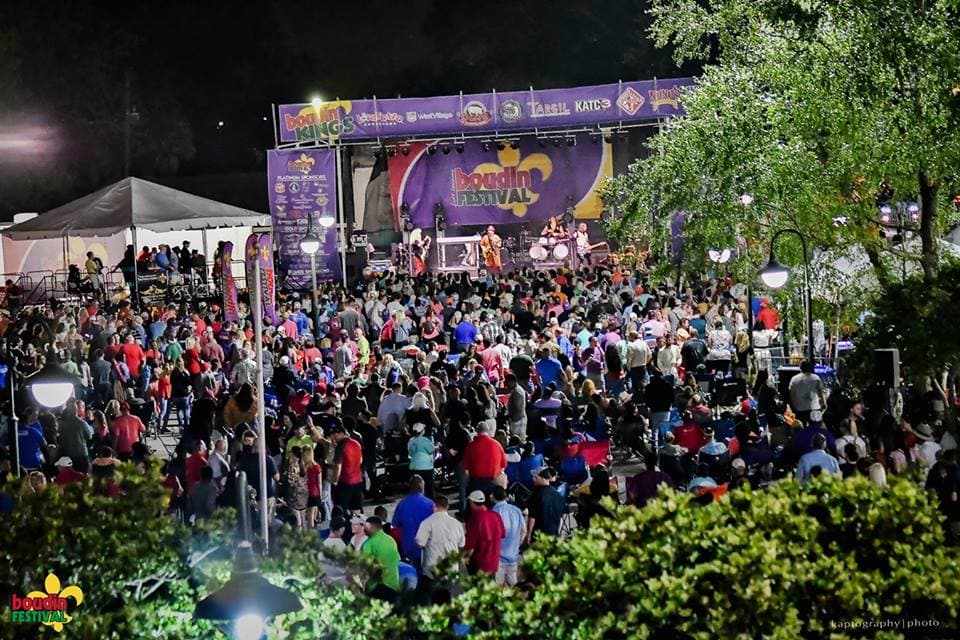A large crowd enjoys a night concert at a festival, with a vibrant stage illuminated in the background.