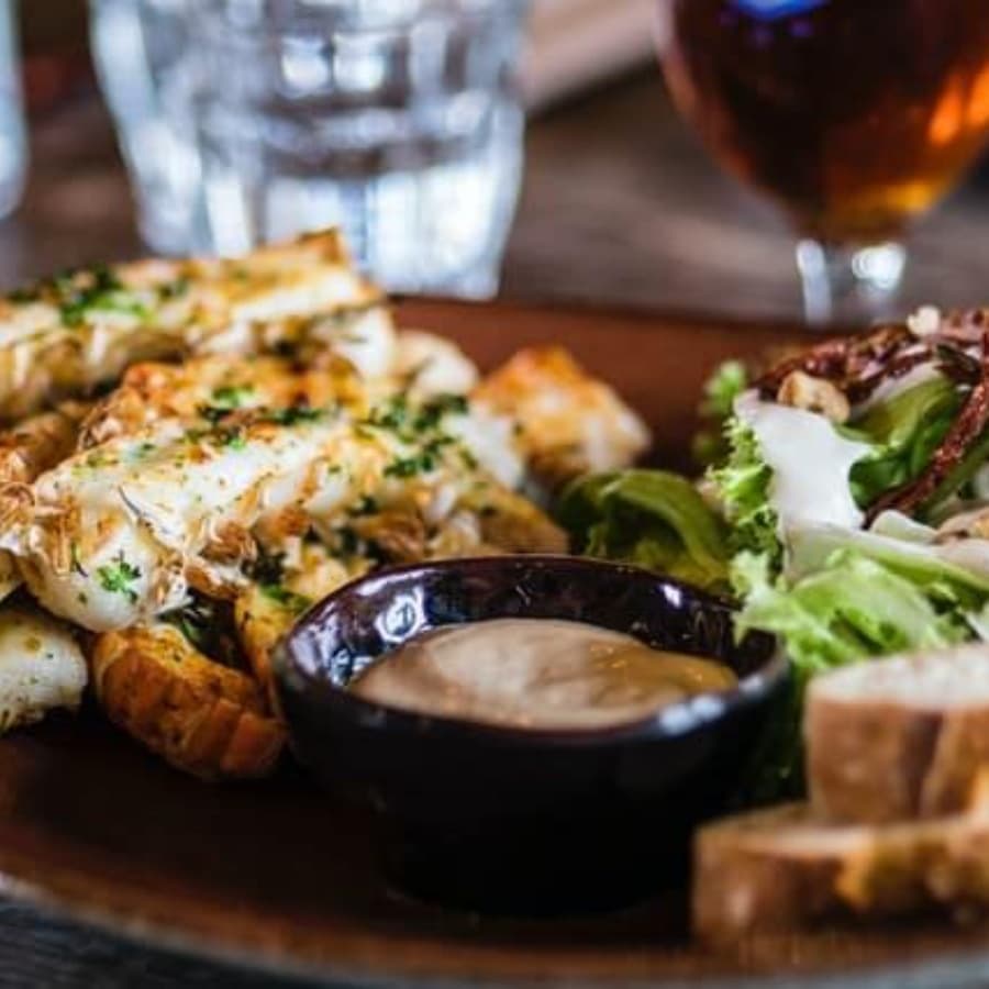 A plate of grilled chicken with herbs, a side salad, and dipping sauce, accompanied by bread.