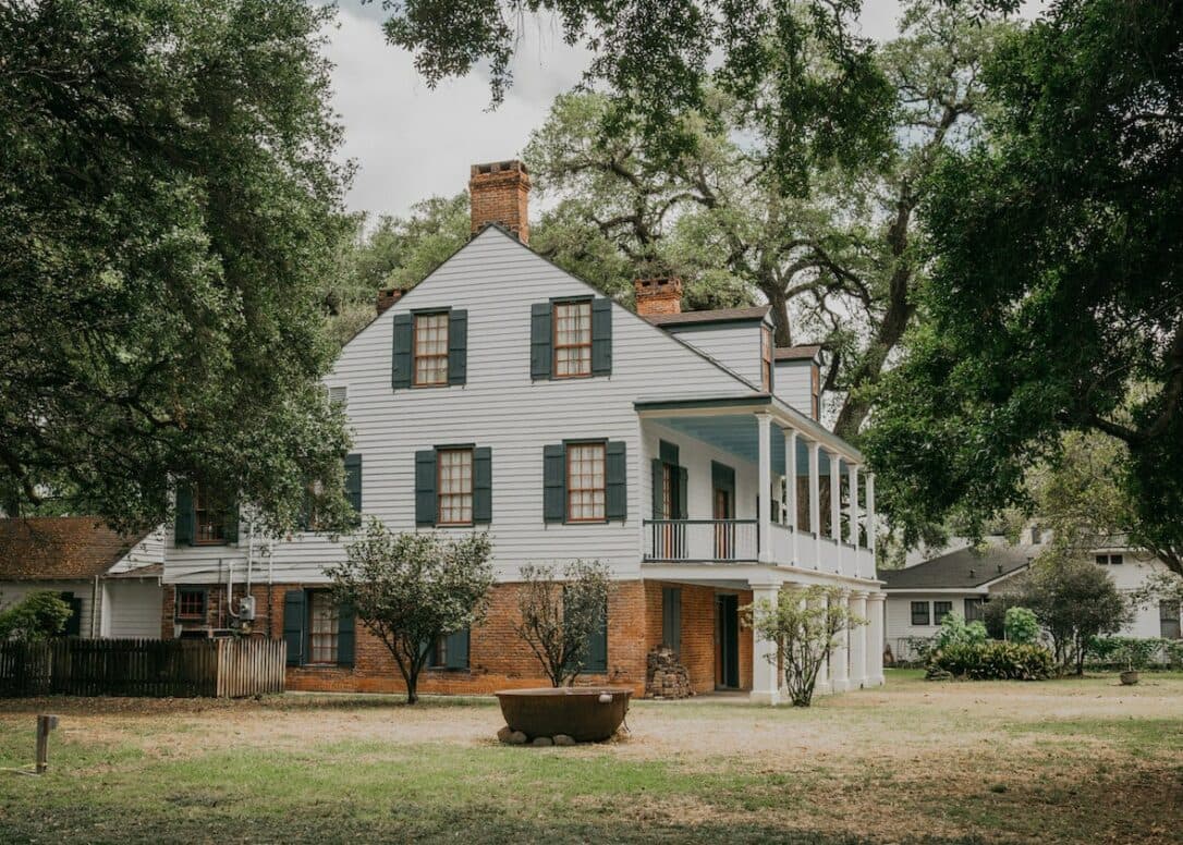 A large, two-story blue and white house surrounded by trees and a grassy yard.