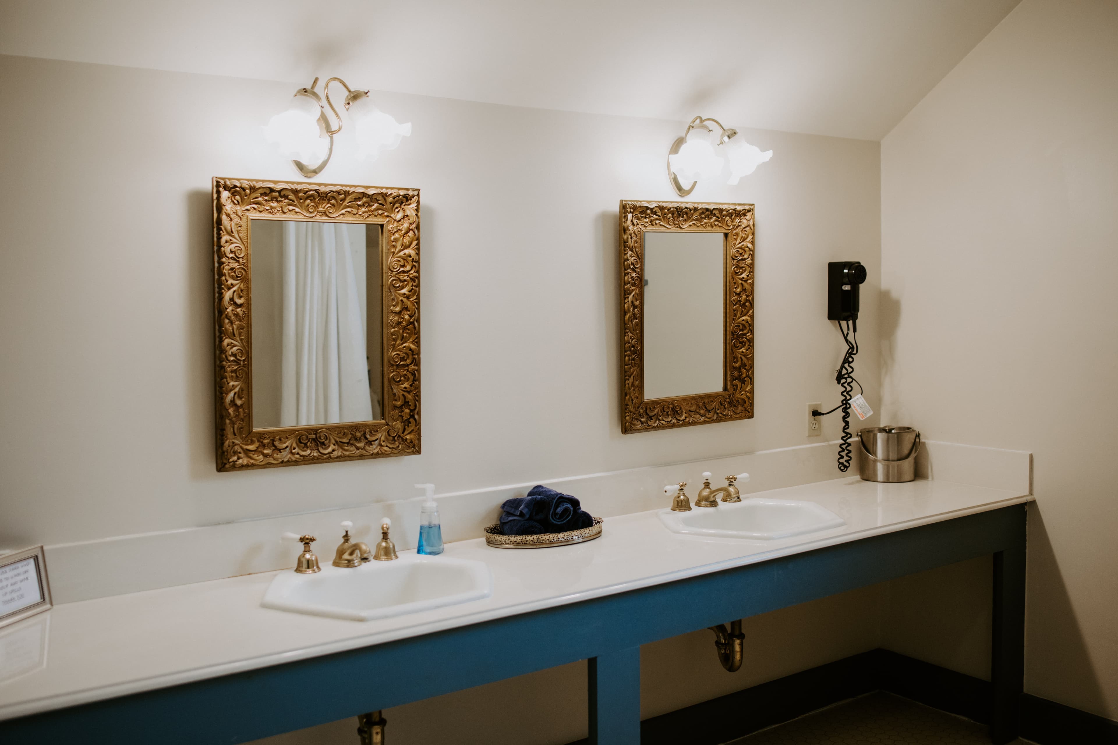 A stylish double vanity with ornate mirrors, a soap dispenser, and towels in a well-lit bathroom.