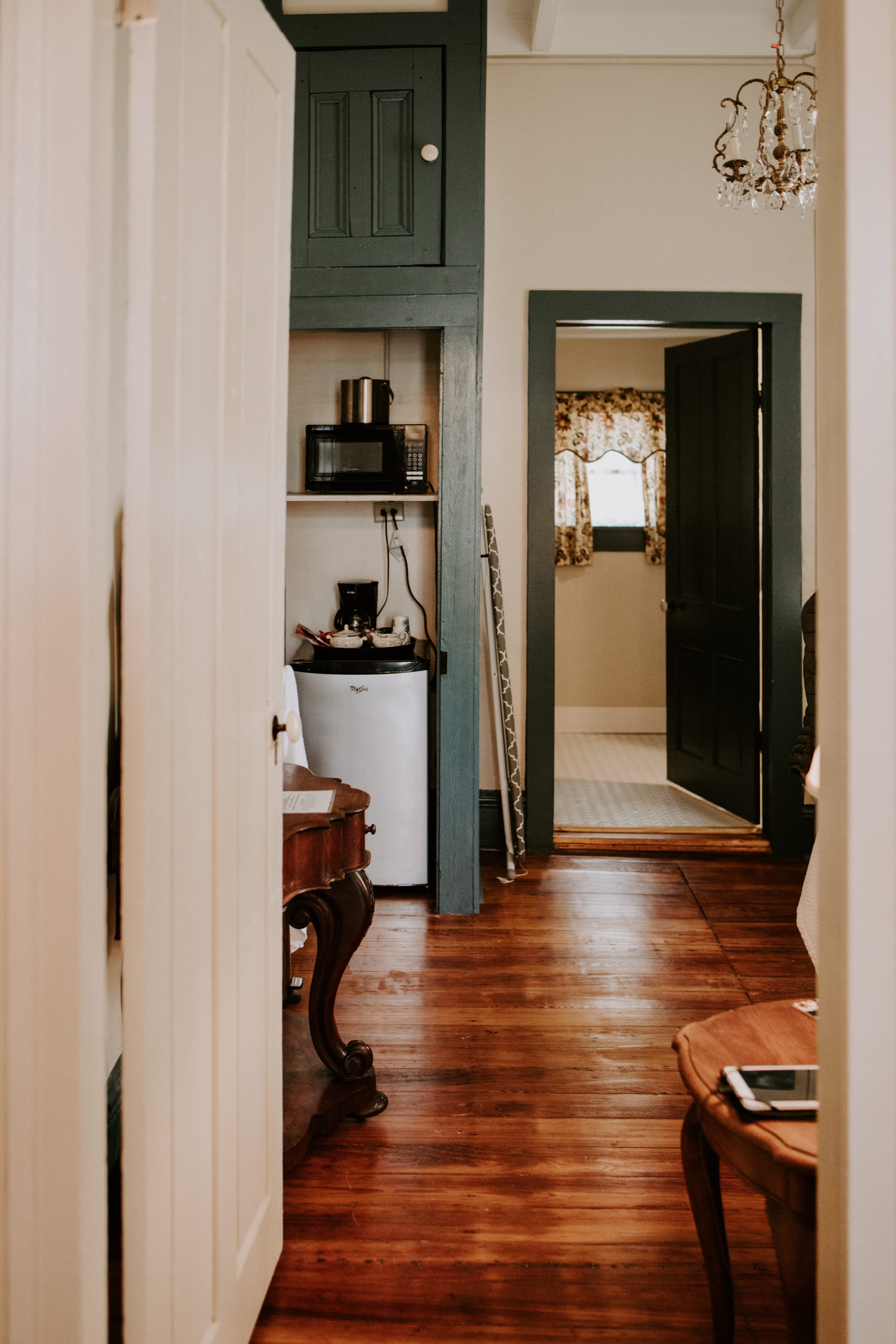A cozy, well-lit hallway leading to a kitchenette and another room, featuring wooden floors and a chandelier.