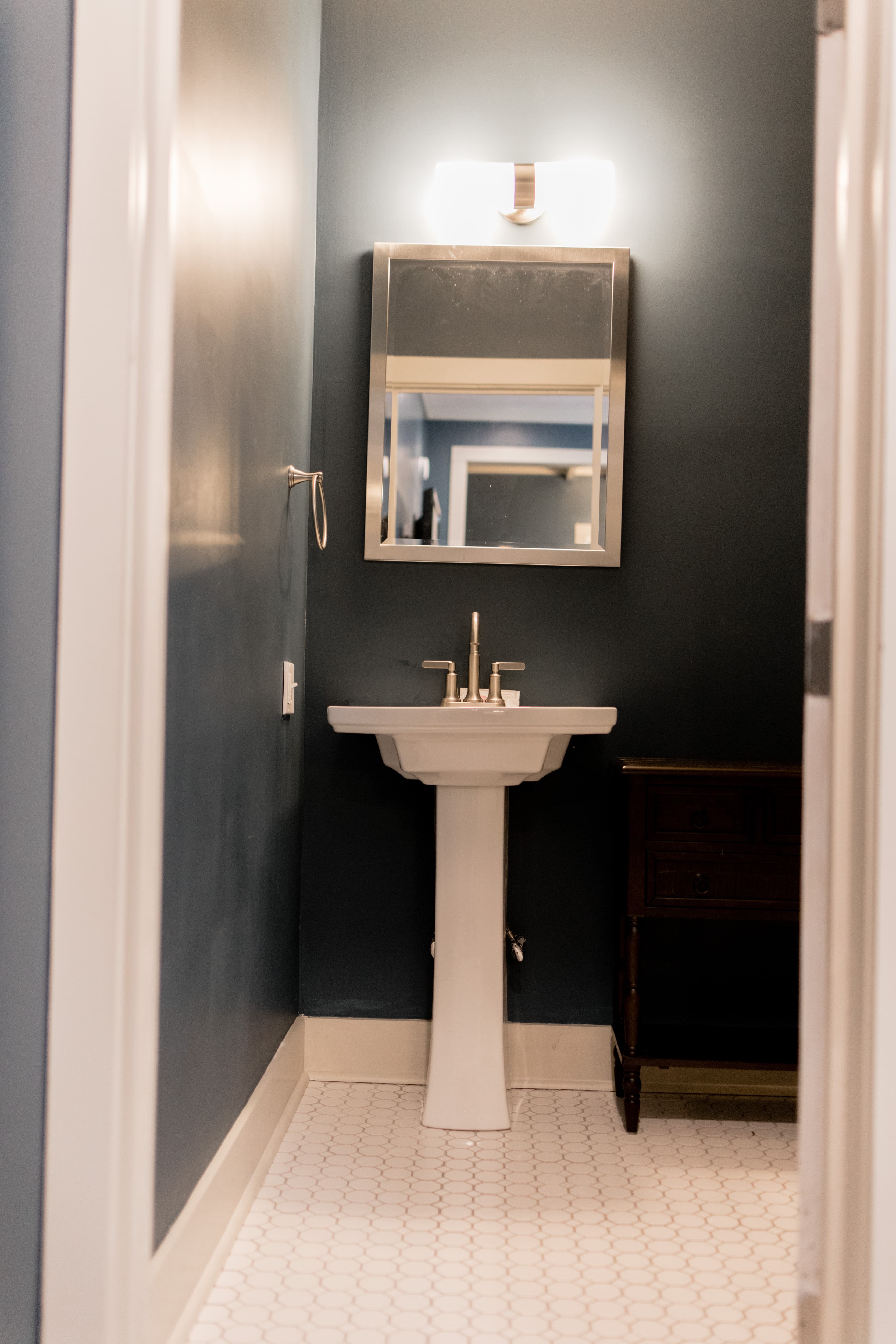 A small bathroom with a pedestal sink, mirror, and dark wall color.