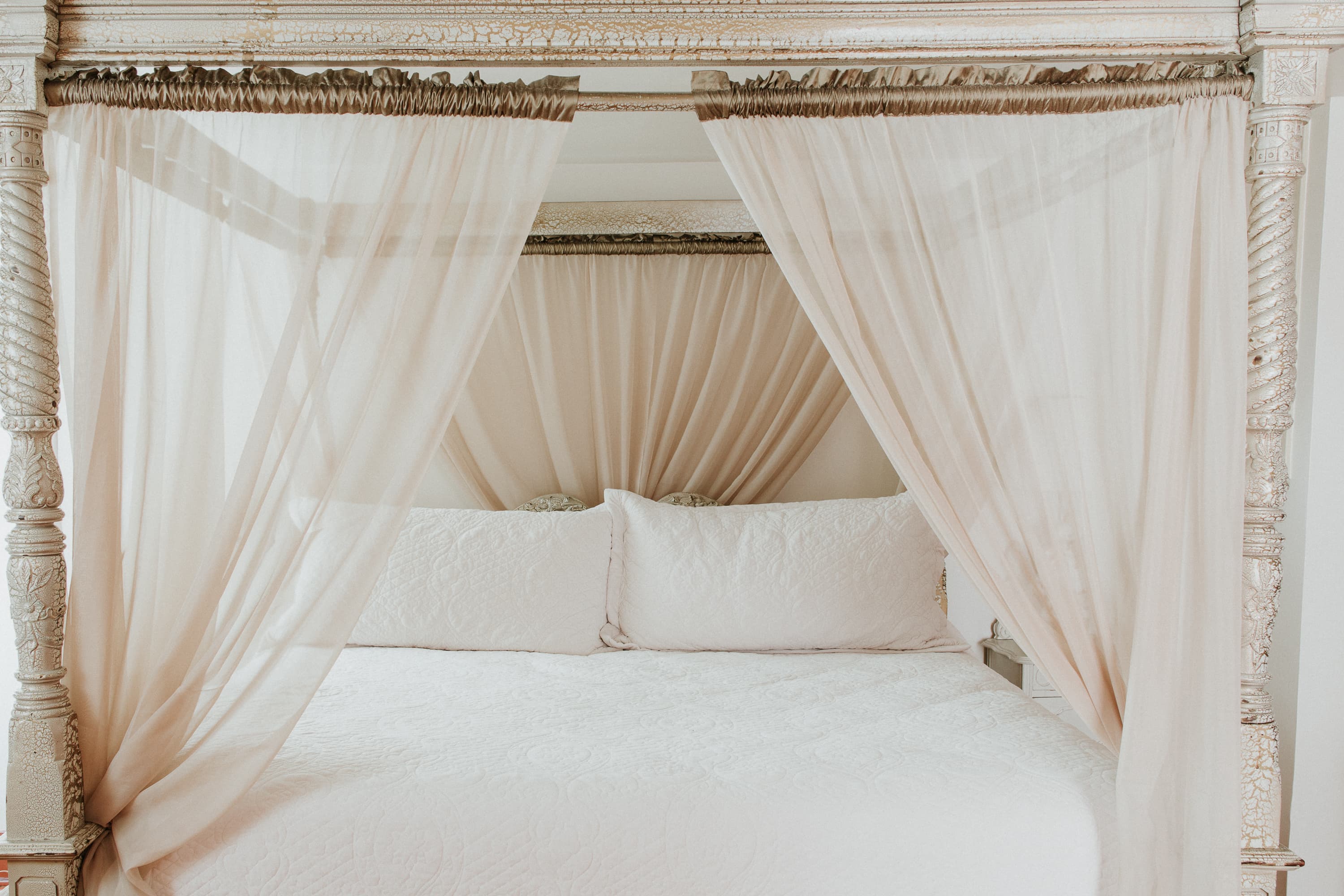 A stylish, light-filled canopy bed with sheer curtains and white bedding.