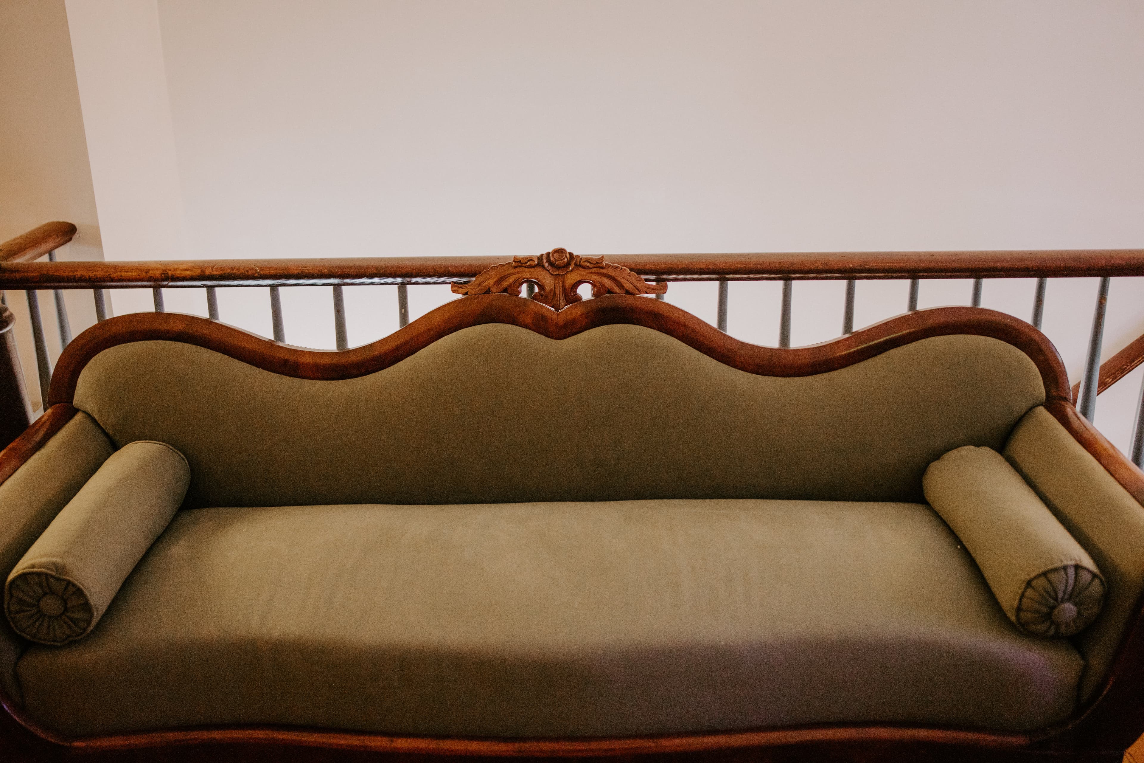 An ornate wooden sofa with a soft green upholstery and decorative armrests.