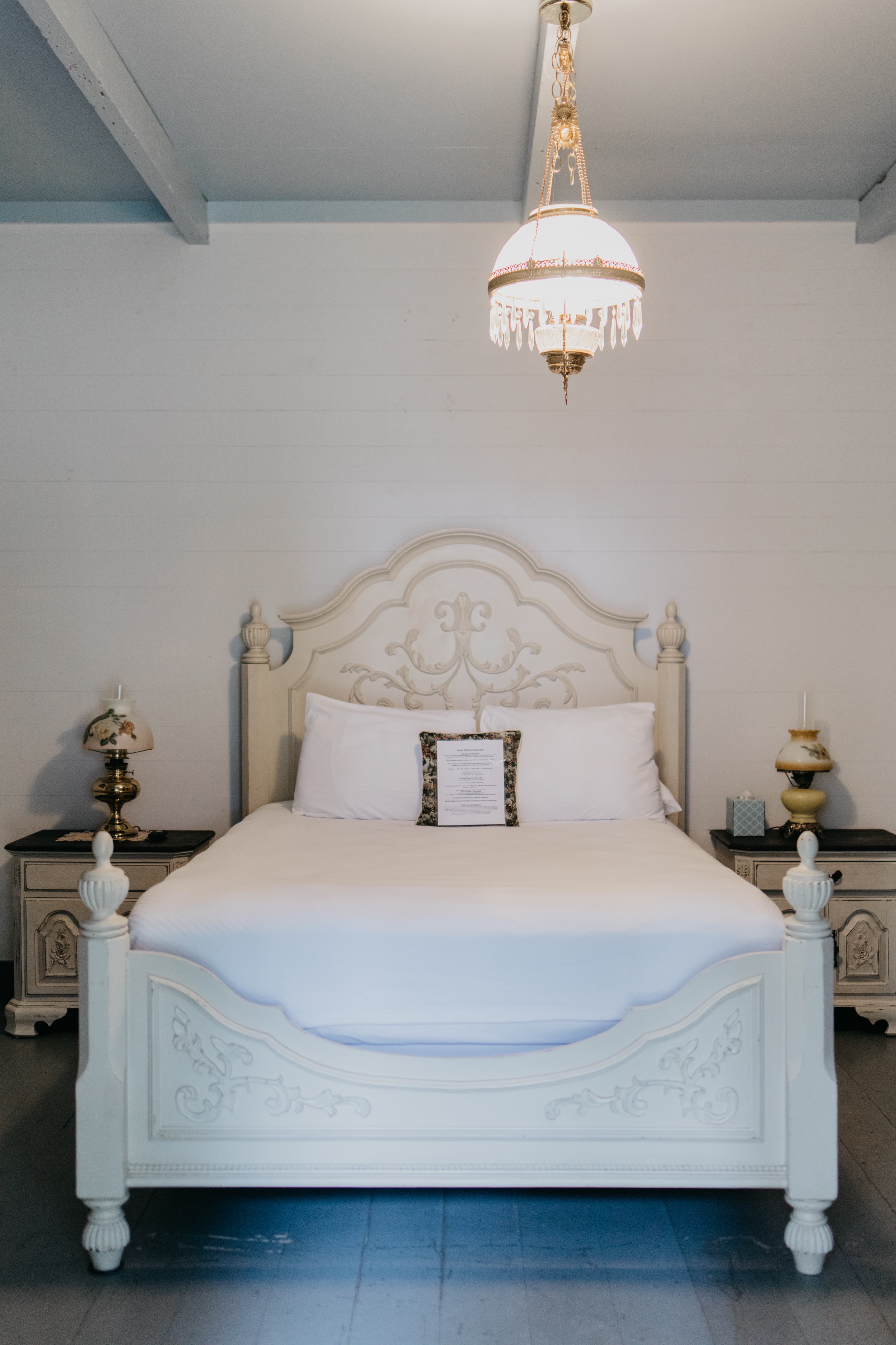 A cozy bedroom featuring a white ornate bed, two bedside tables with lamps, and a chandelier overhead.
