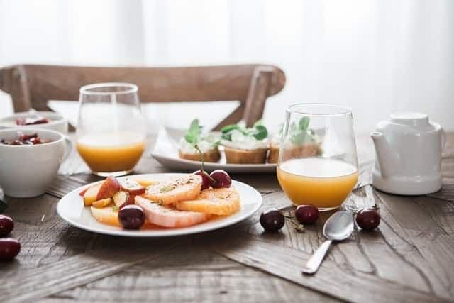 A wooden table set with a plate of fresh fruit, two glasses of juice, and small bowls of yogurt and muffins.