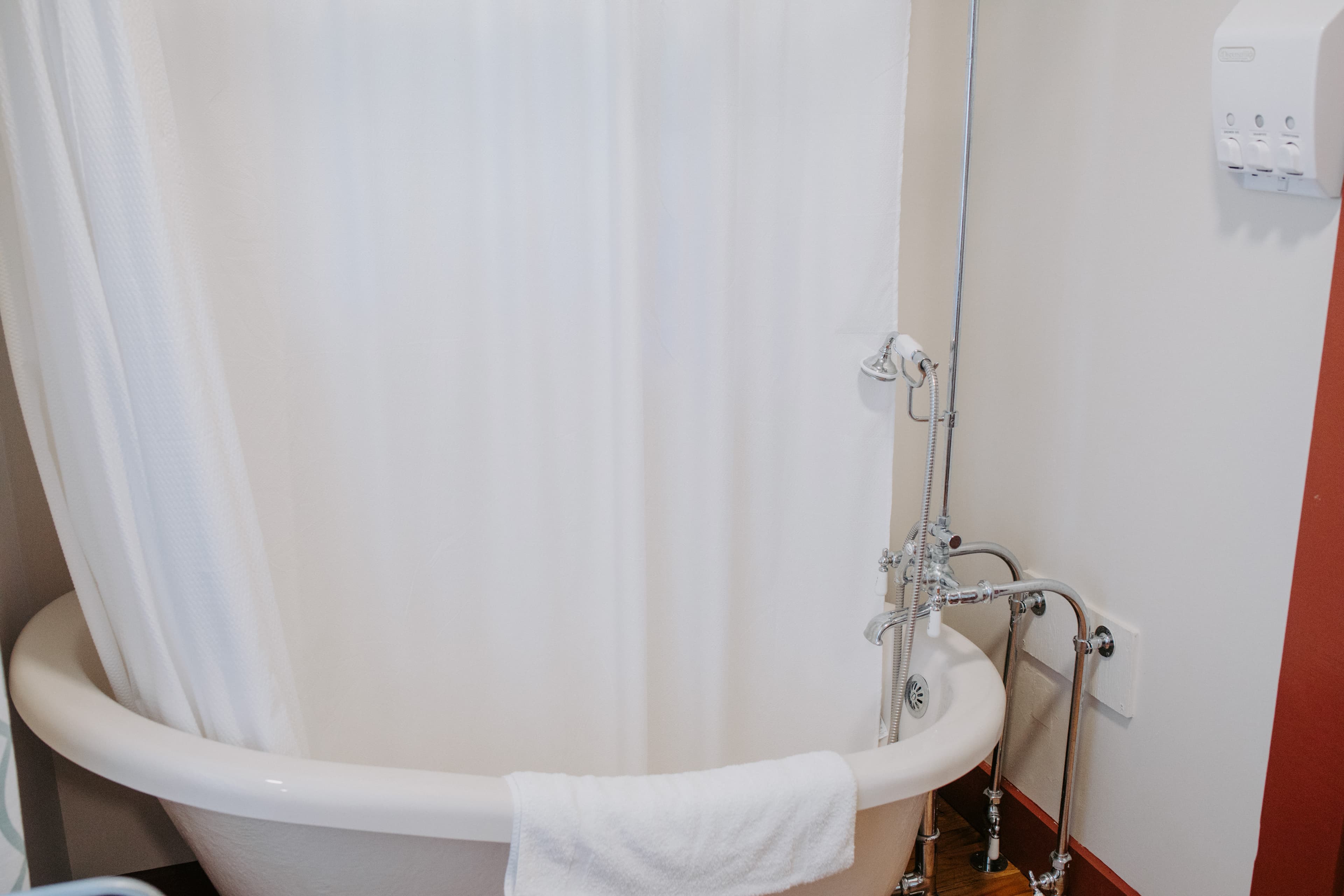 A vintage-style bathtub with a shower curtain and a towel hanging over the edge.