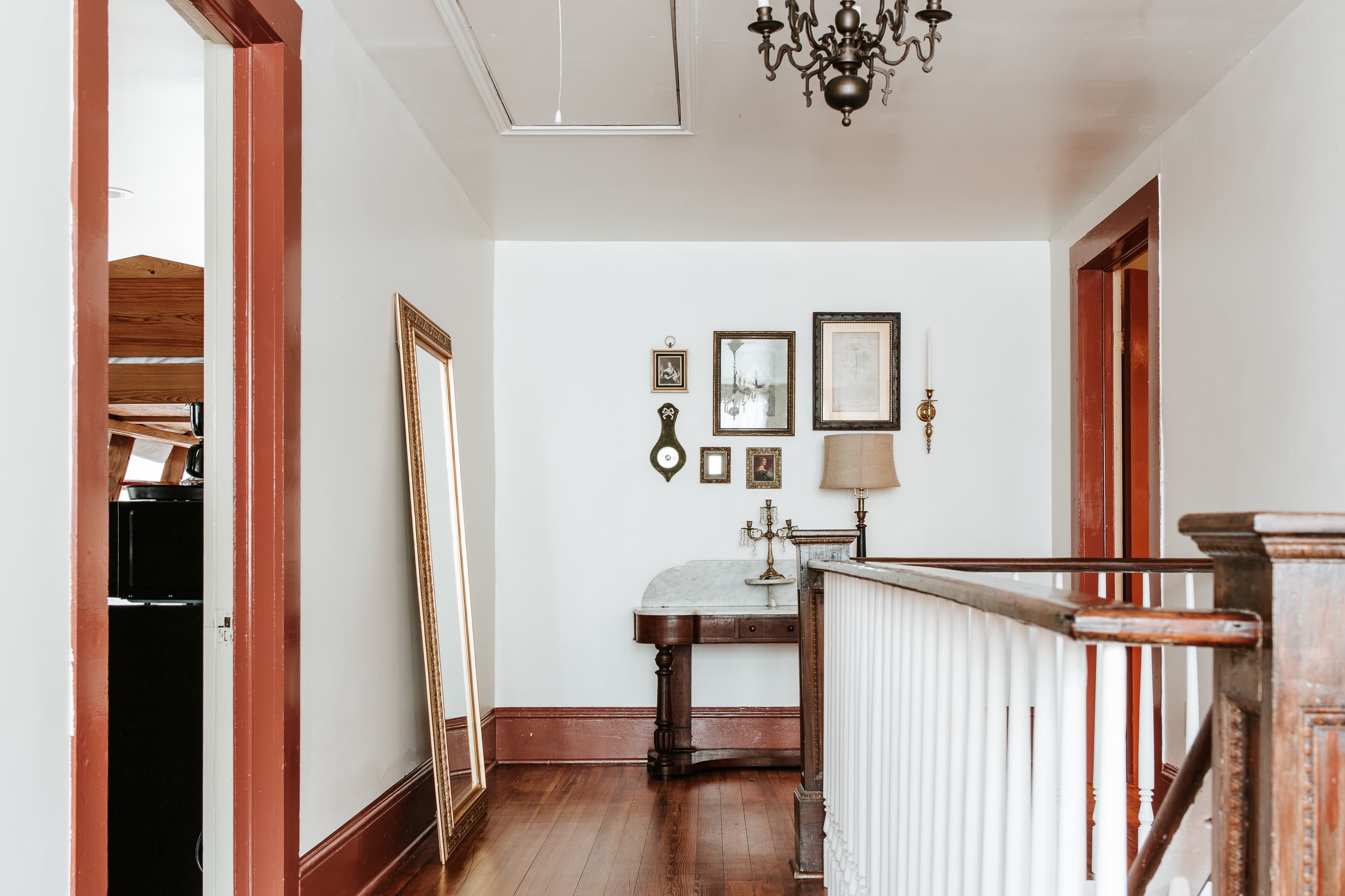 A well-lit hallway featuring a mirror, framed artwork, and a vintage table with a lamp.