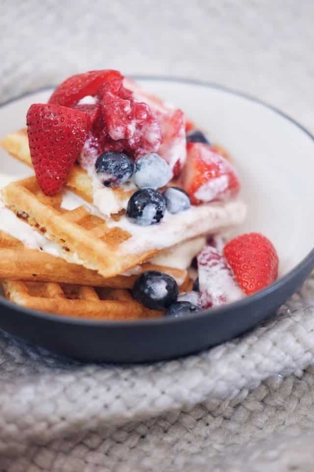 A bowl of waffles topped with strawberries, blueberries, and whipped cream.