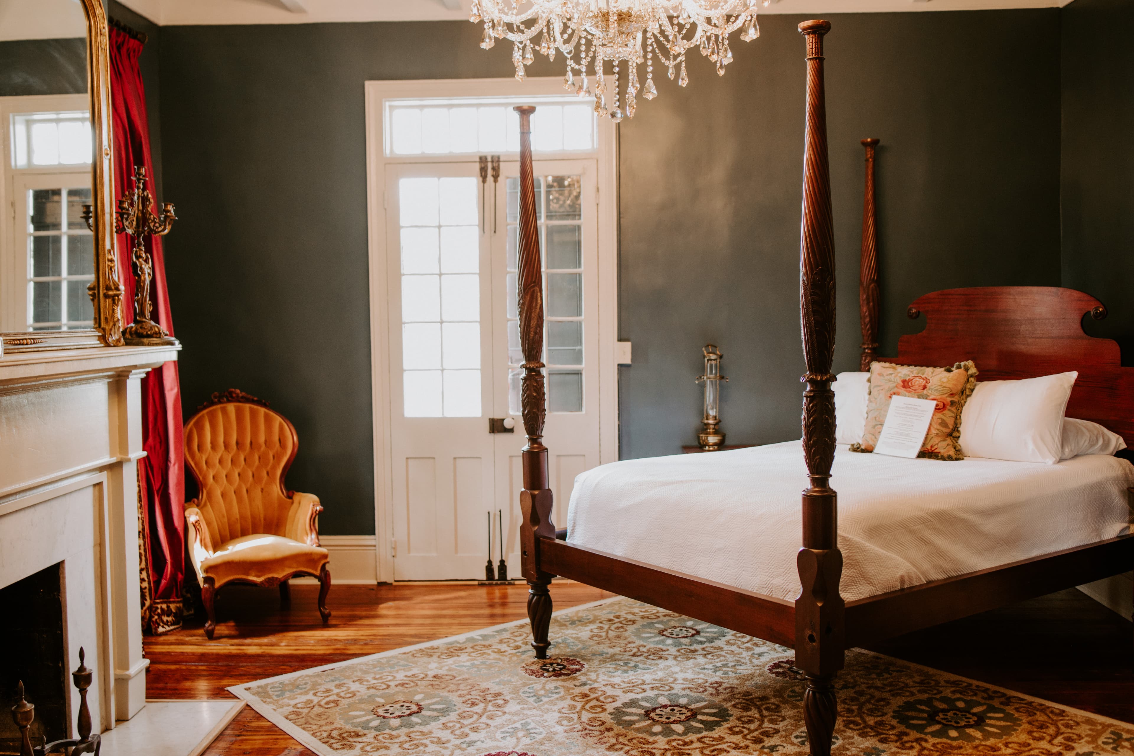 A cozy bedroom featuring a four-poster bed, a vintage armchair, and elegant decor under a chandelier.