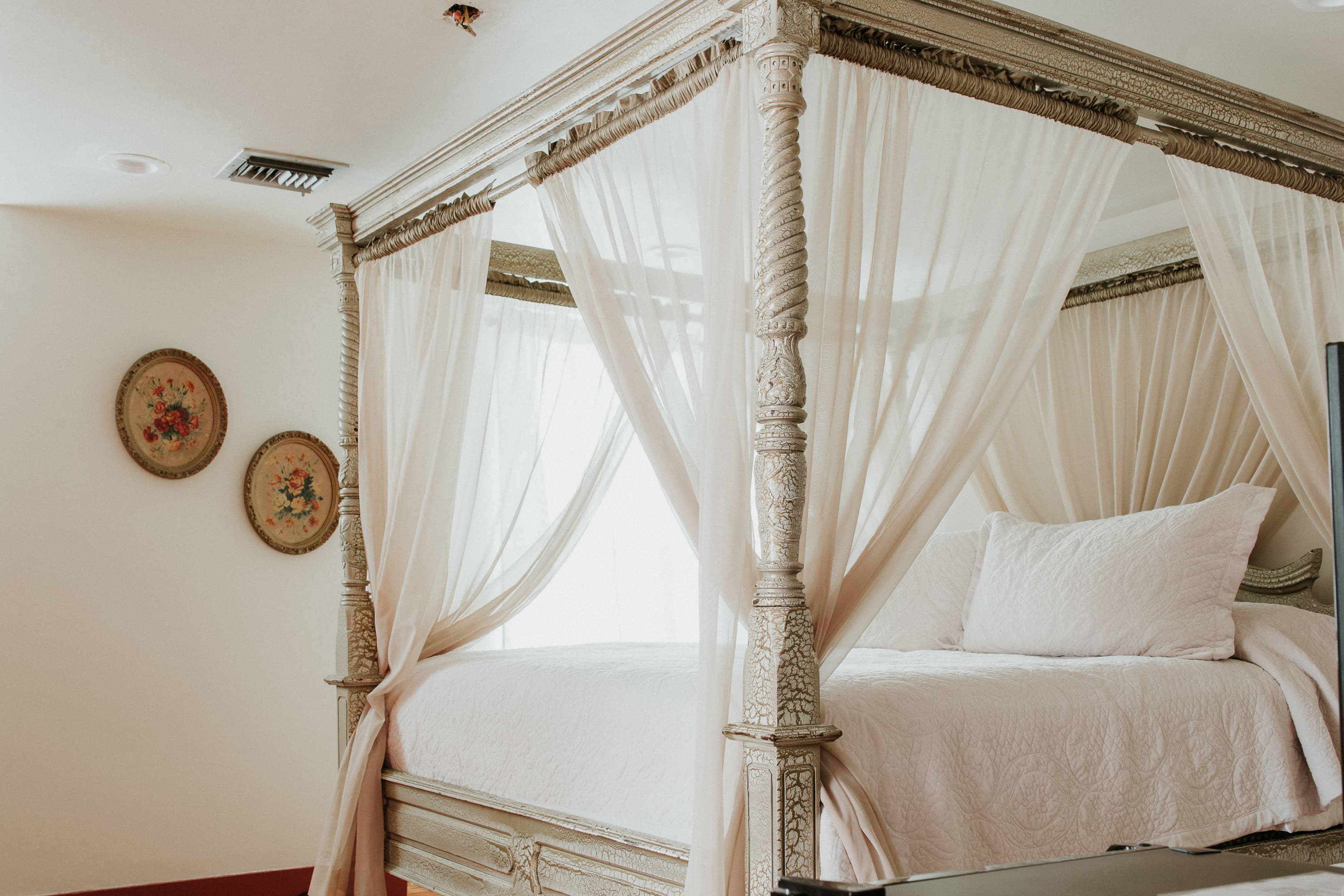 A beautifully draped canopy bed in a softly lit room with decorative wall plates.