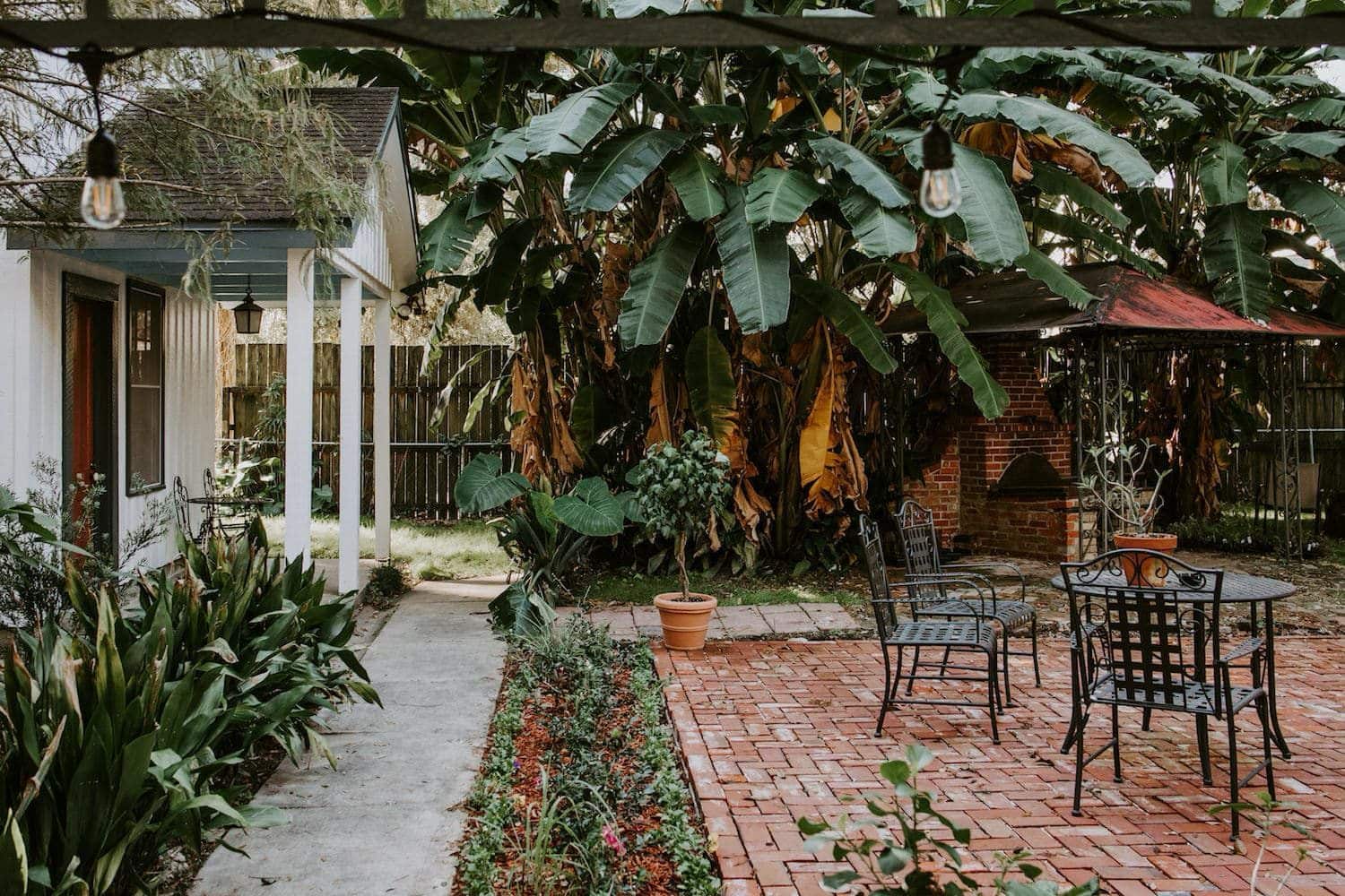A cozy outdoor patio with a brick walkway, surrounded by lush greenery and banana trees.