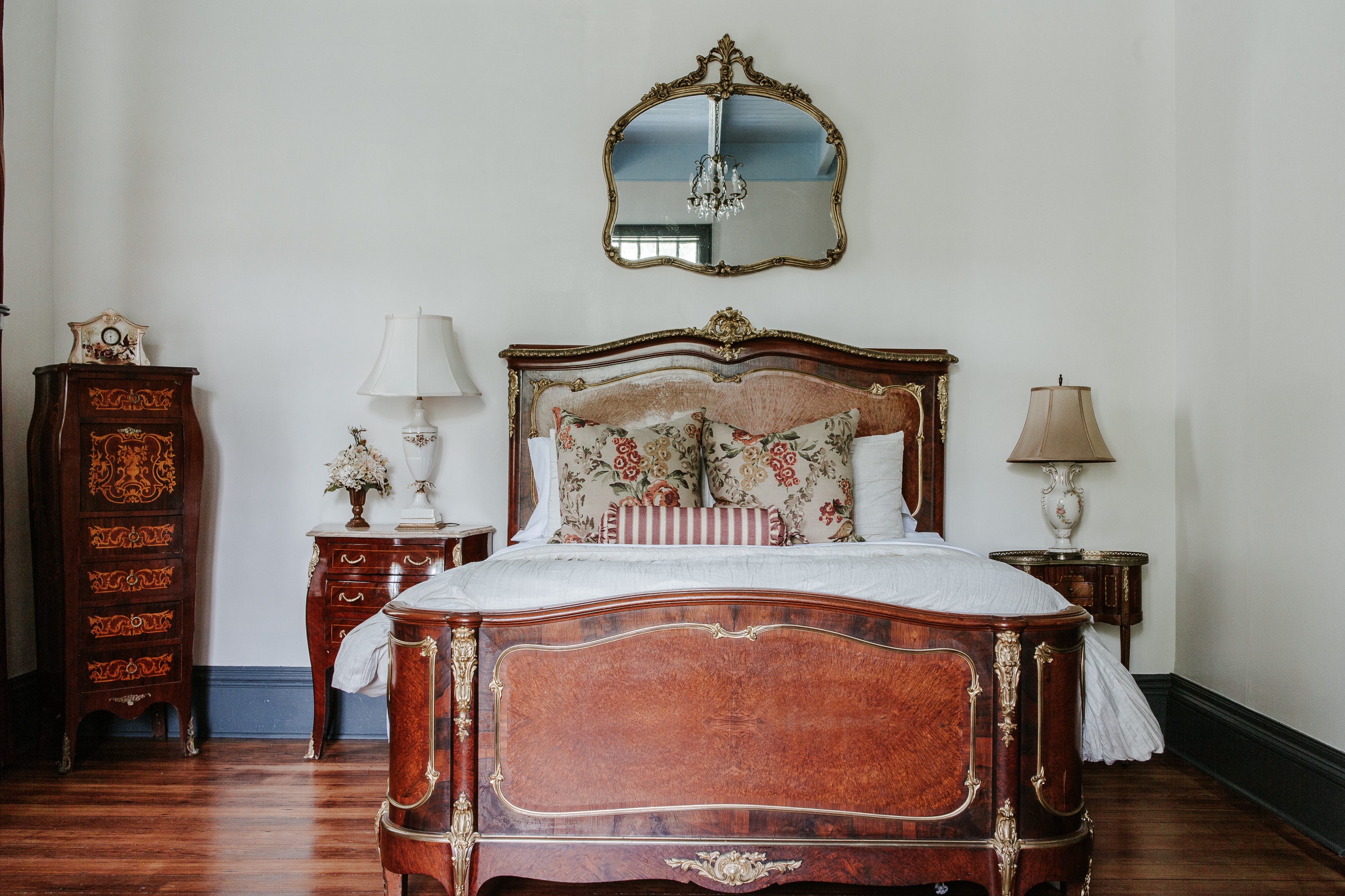 A vintage-style bedroom featuring an ornate wooden bed, decorative pillows, and antique furniture.