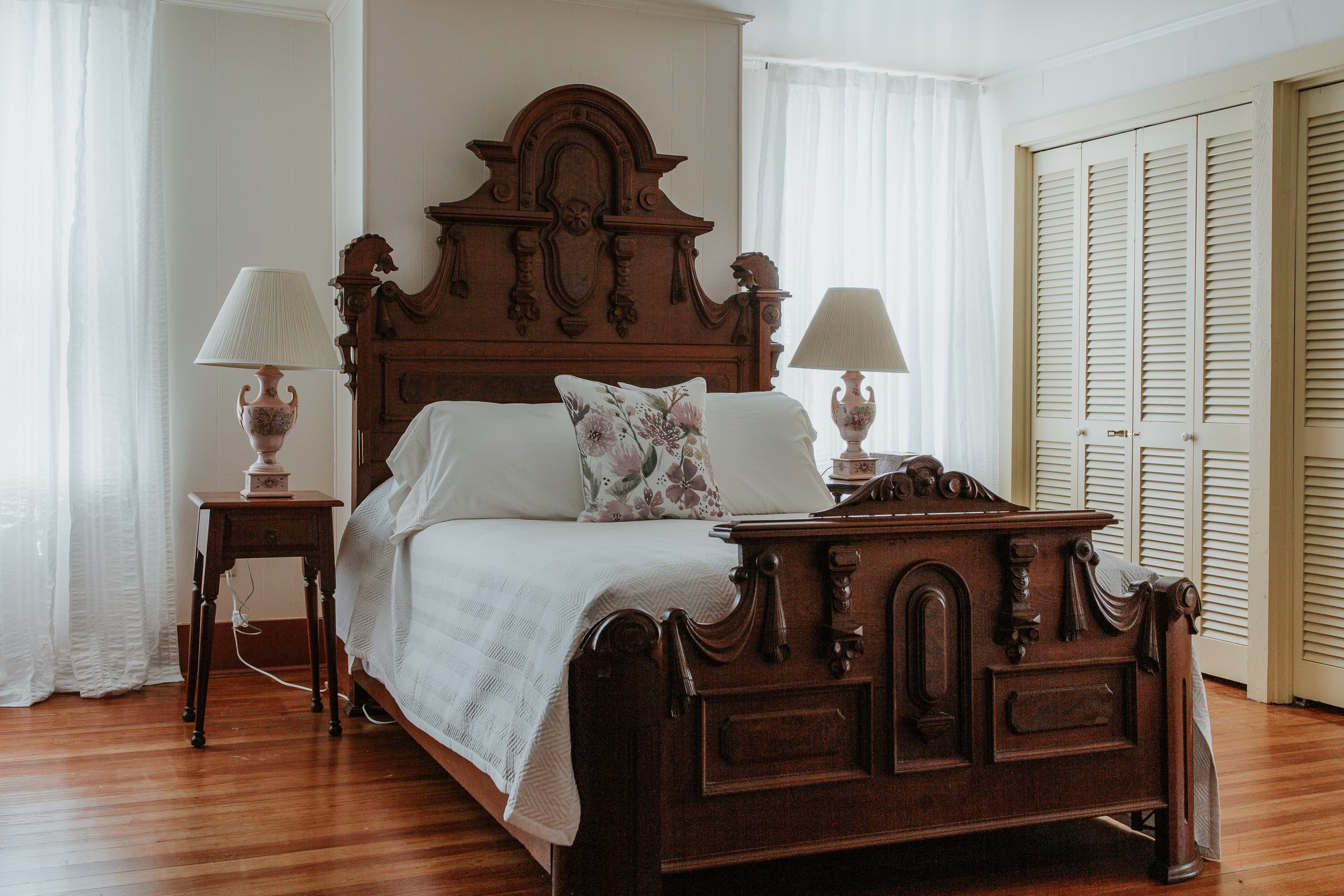 A vintage wooden bed with ornate headboard and two bedside lamps in a softly lit bedroom.