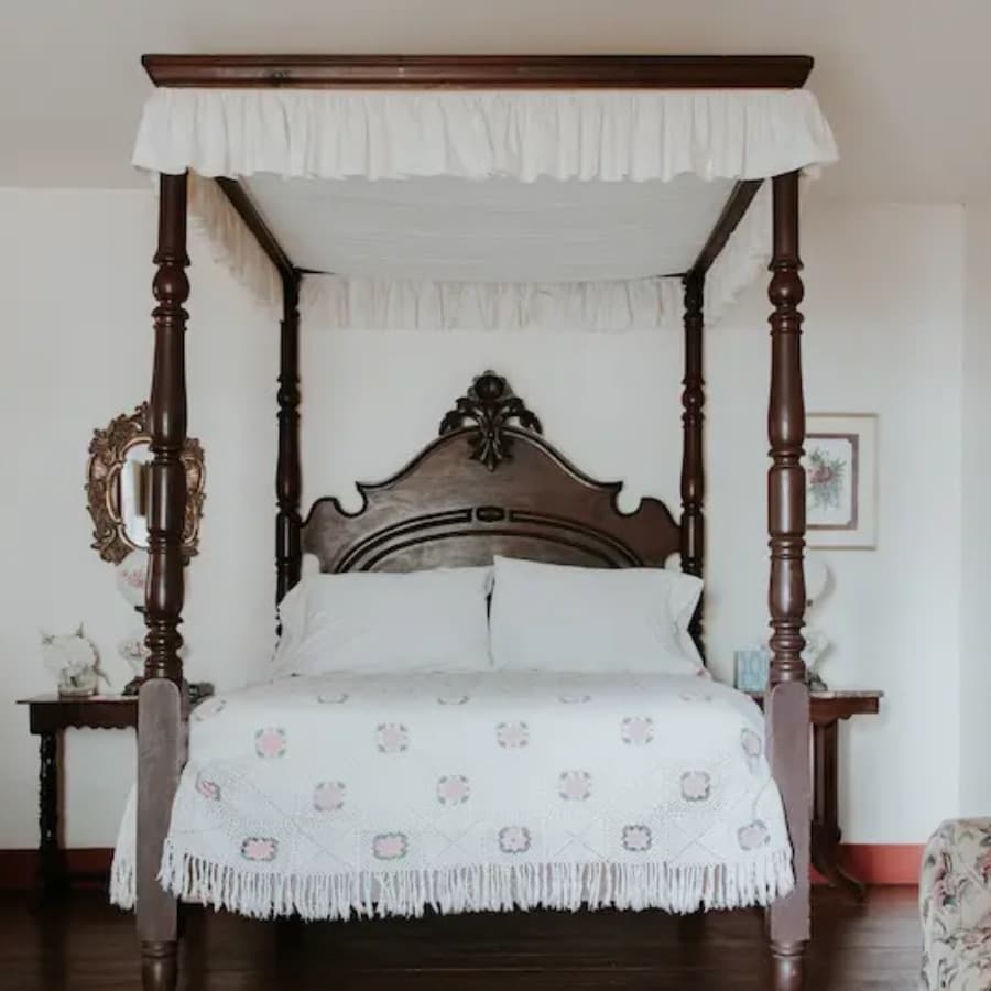A vintage four-poster bed with a white canopy and floral-patterned blanket in a softly lit room.