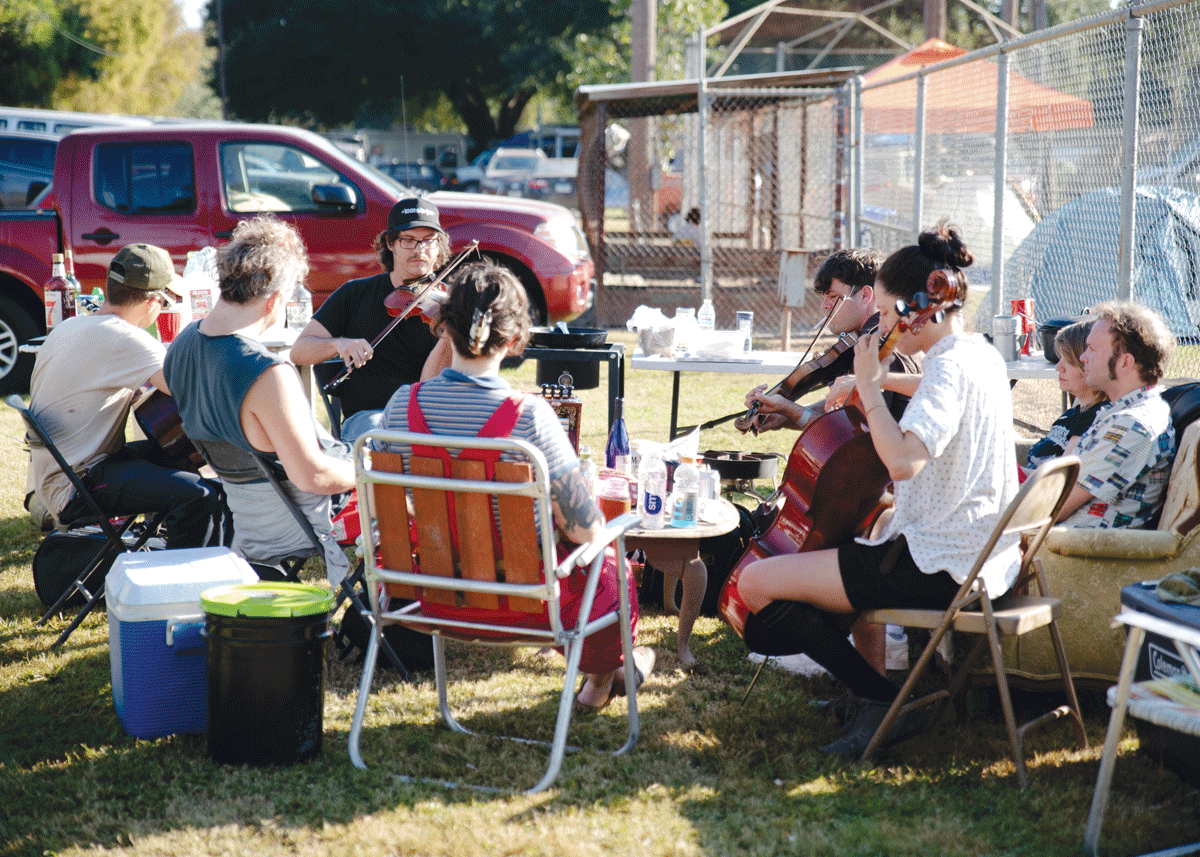 A group of musicians sits outdoors in a circle, playing various string instruments.