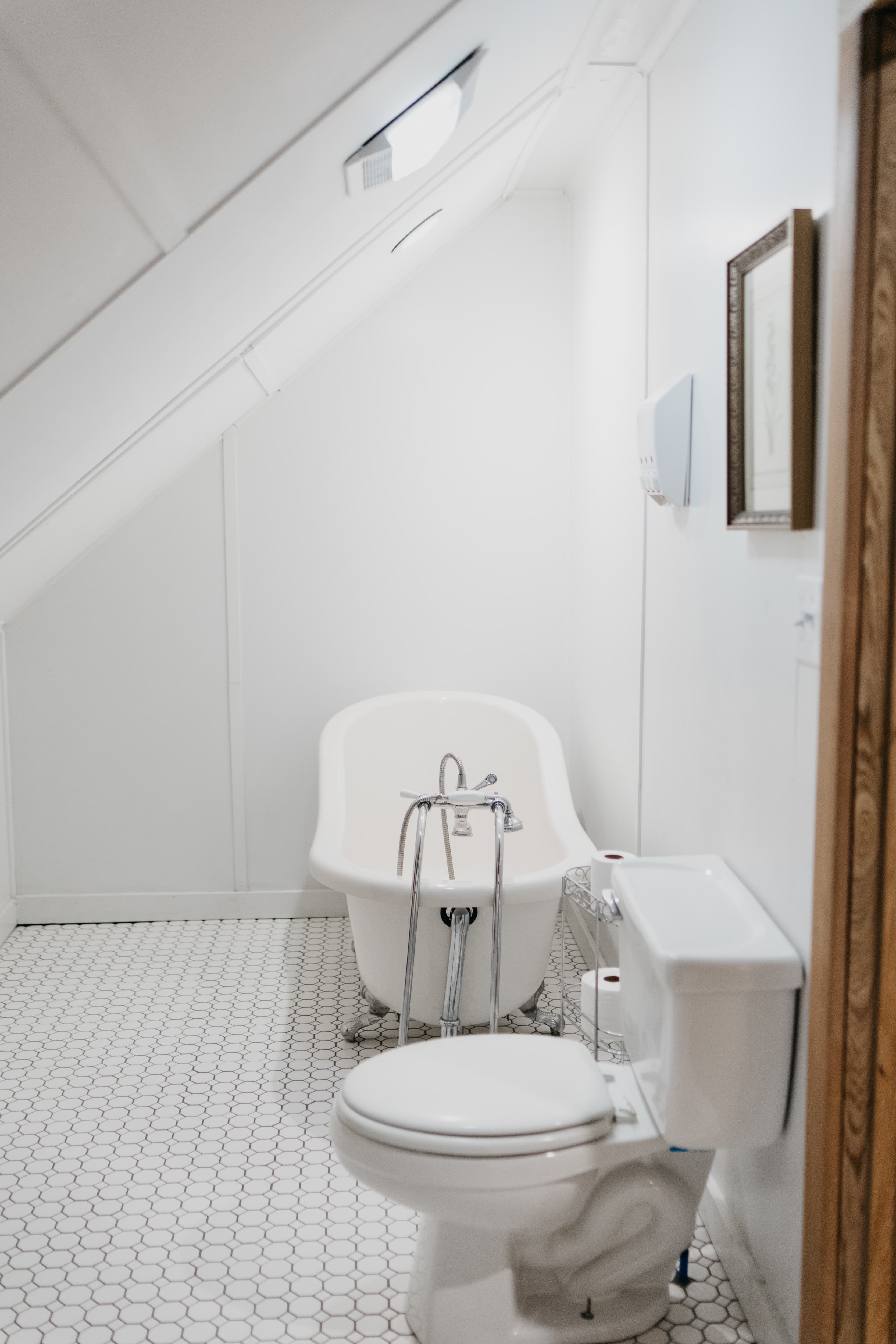 A minimalistic bathroom with a bathtub and toilet under an angled ceiling.