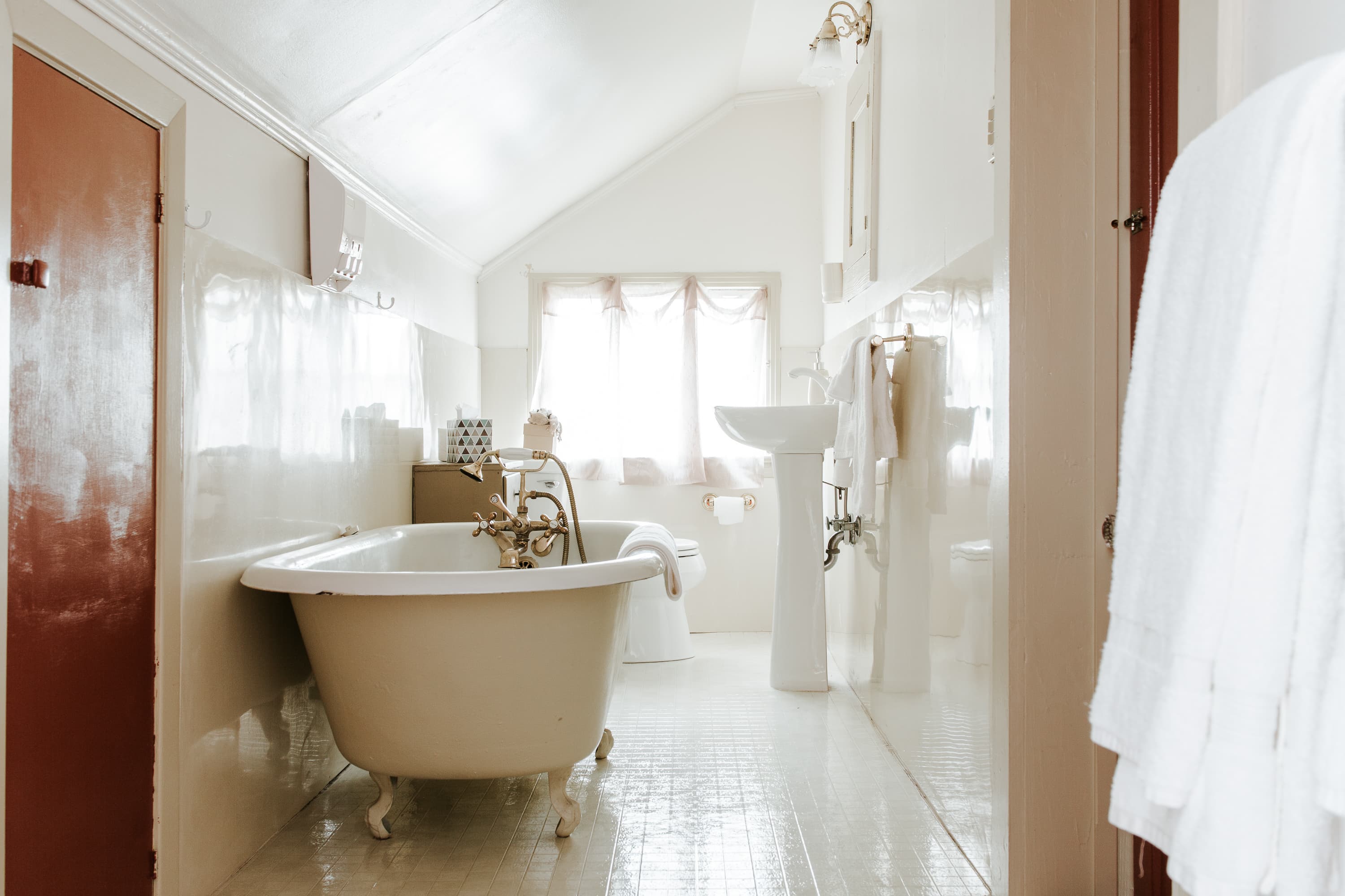 A bright, minimalist bathroom featuring a freestanding tub, pedestal sink, and natural light streaming through a window.