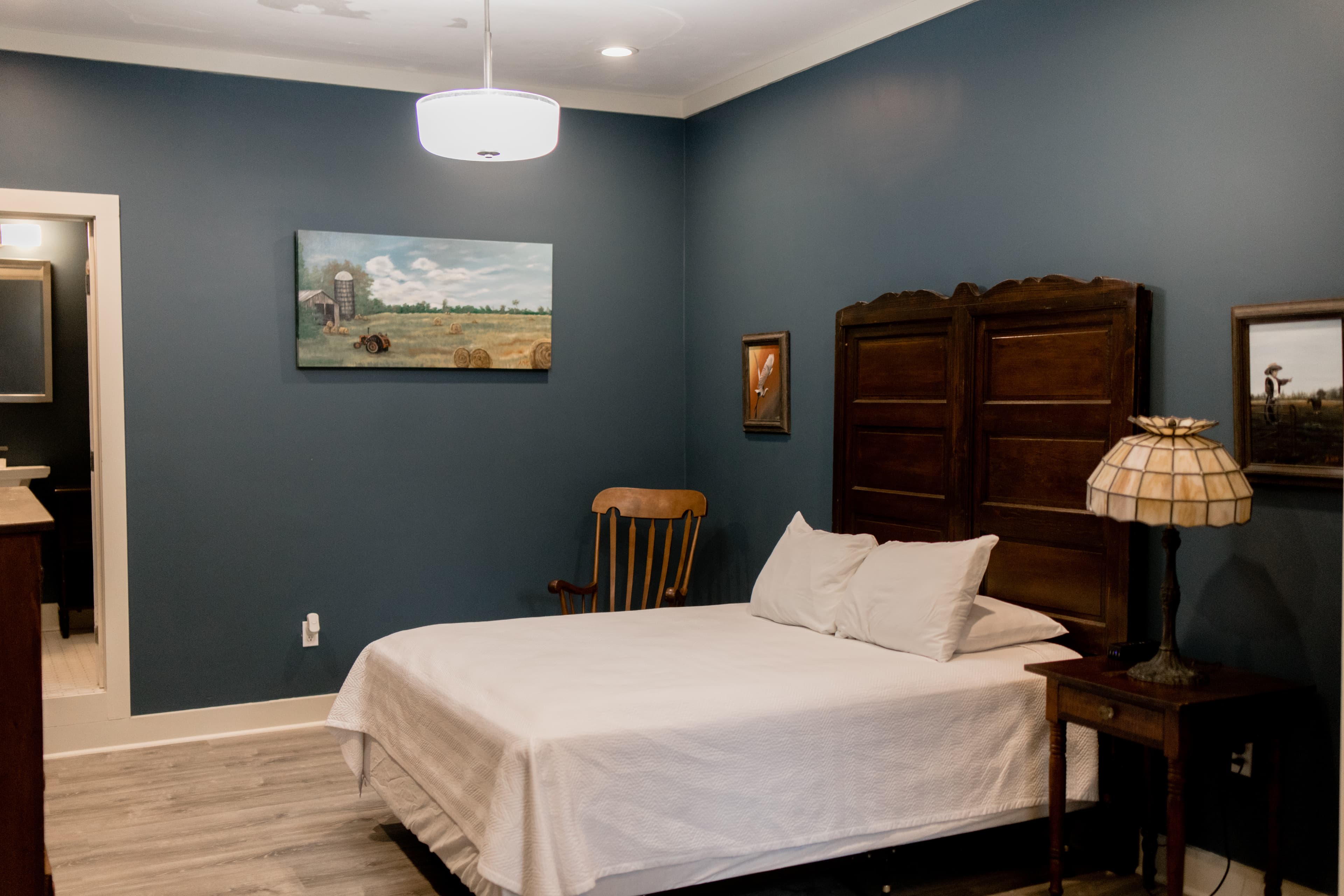 Cozy bedroom featuring a bed, wooden accents, and blue walls with a landscape painting.