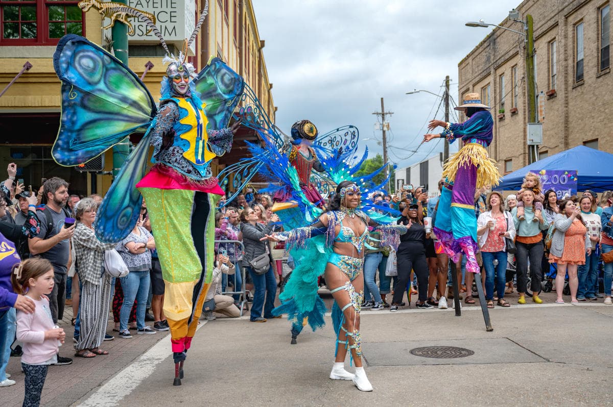 A lively street parade features performers in vibrant, butterfly-themed costumes, entertaining a diverse crowd.