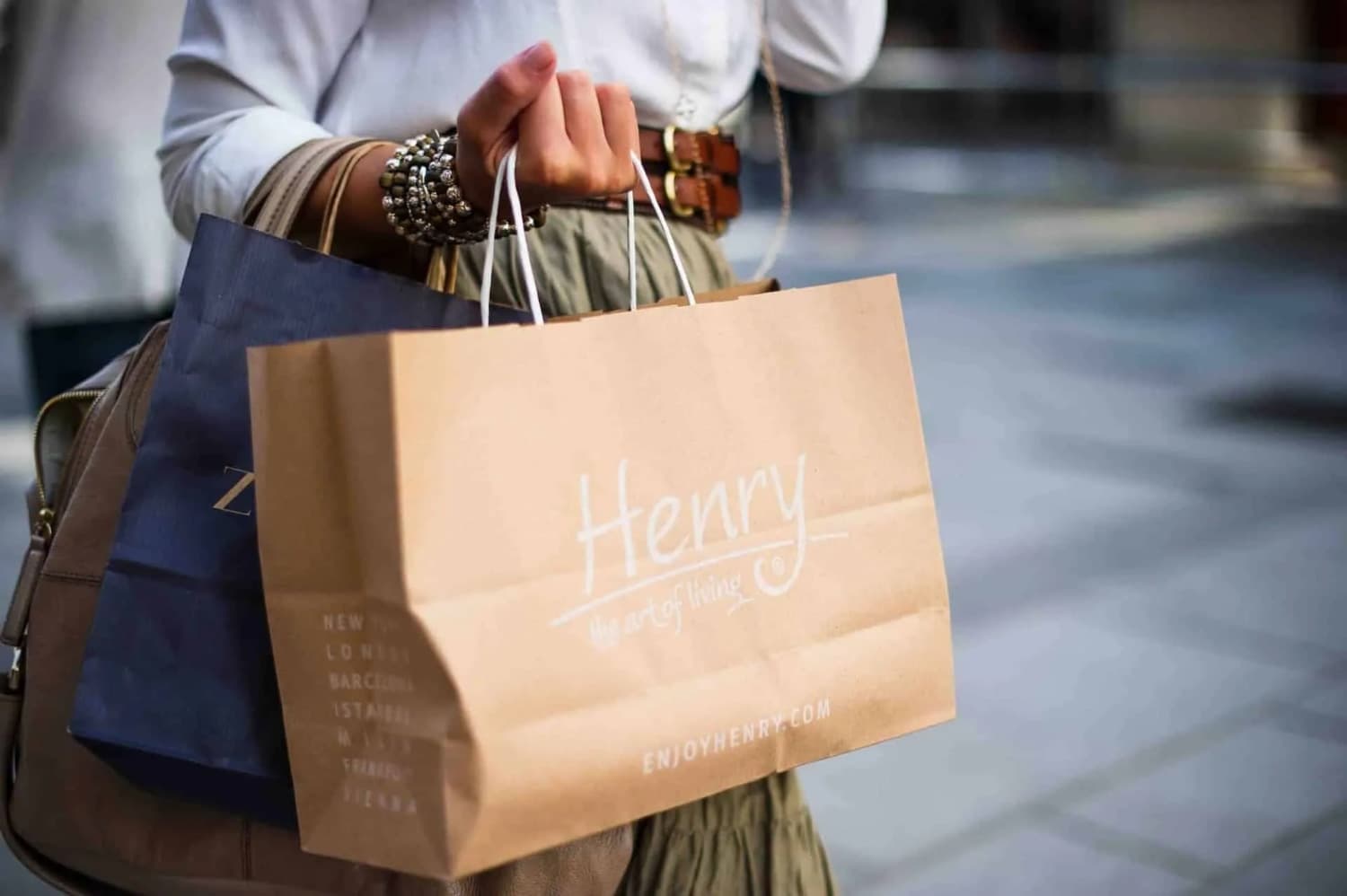 A person is carrying a brown shopping bag with the name "Henry" printed on it.