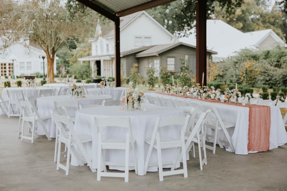 A beautifully arranged outdoor event space with white tables, chairs, and floral centerpieces.