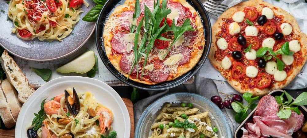 An assortment of pasta dishes and pizzas garnished with fresh ingredients.