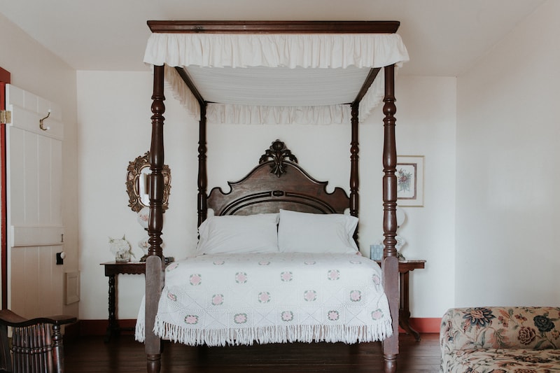 A cozy four-poster bed with a white quilt and decorative pillows in a softly lit room.