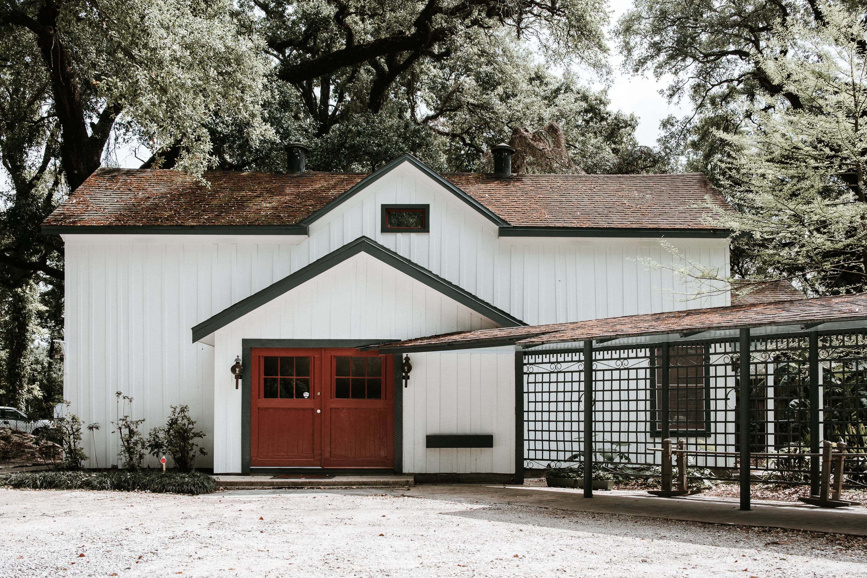 A white farmhouse with a red door surrounded by trees and a trellis.