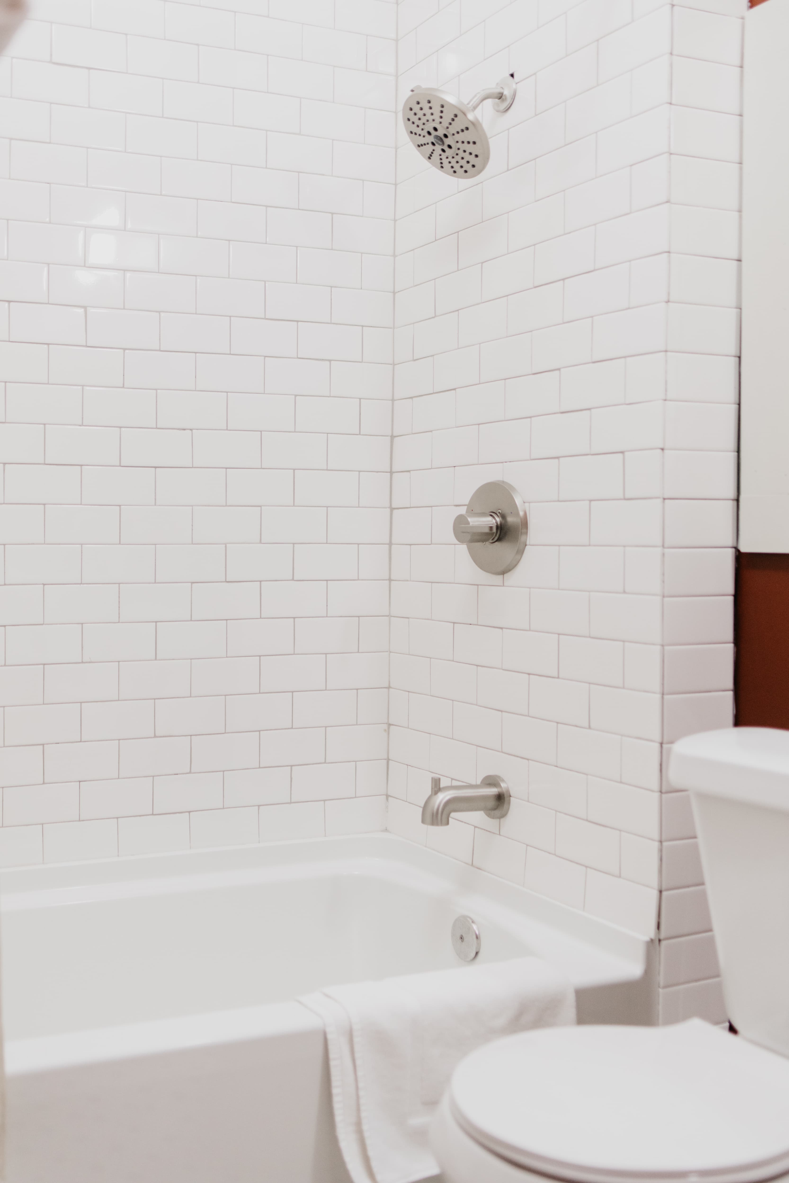 A modern bathroom featuring a white tiled shower and bathtub with a towel draped over the edge.