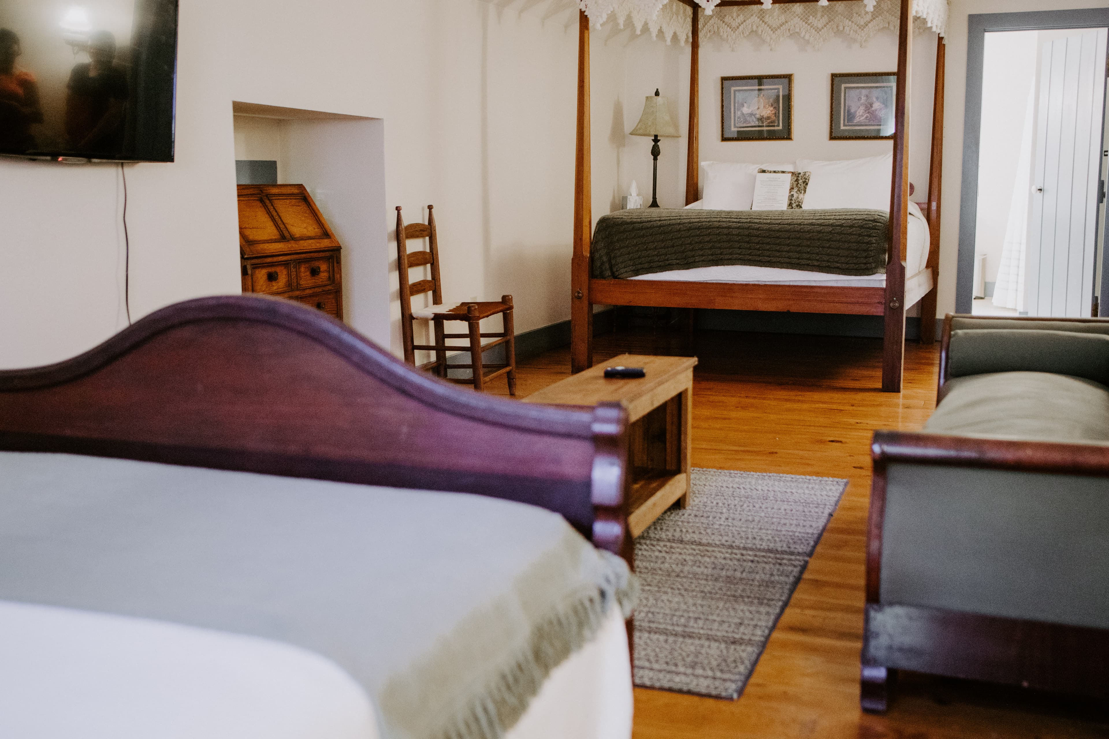 A cozy bedroom featuring a four-poster bed, a wooden chair, and a television.