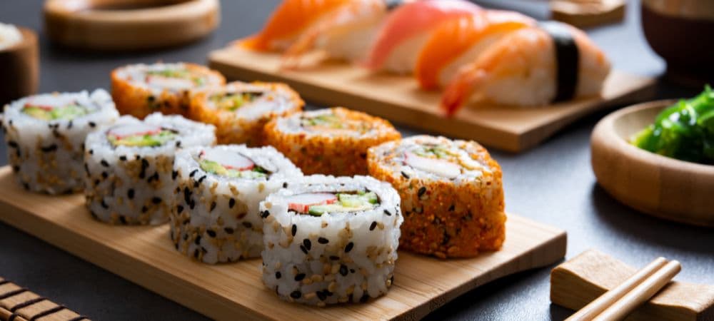 A wooden plate holding various sushi rolls and sashimi, with chopsticks beside it.