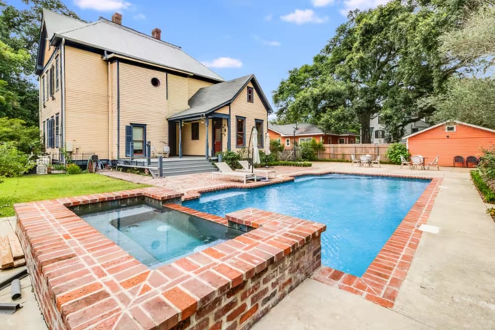 A spacious backyard featuring a swimming pool and a hot tub beside a large two-story house.