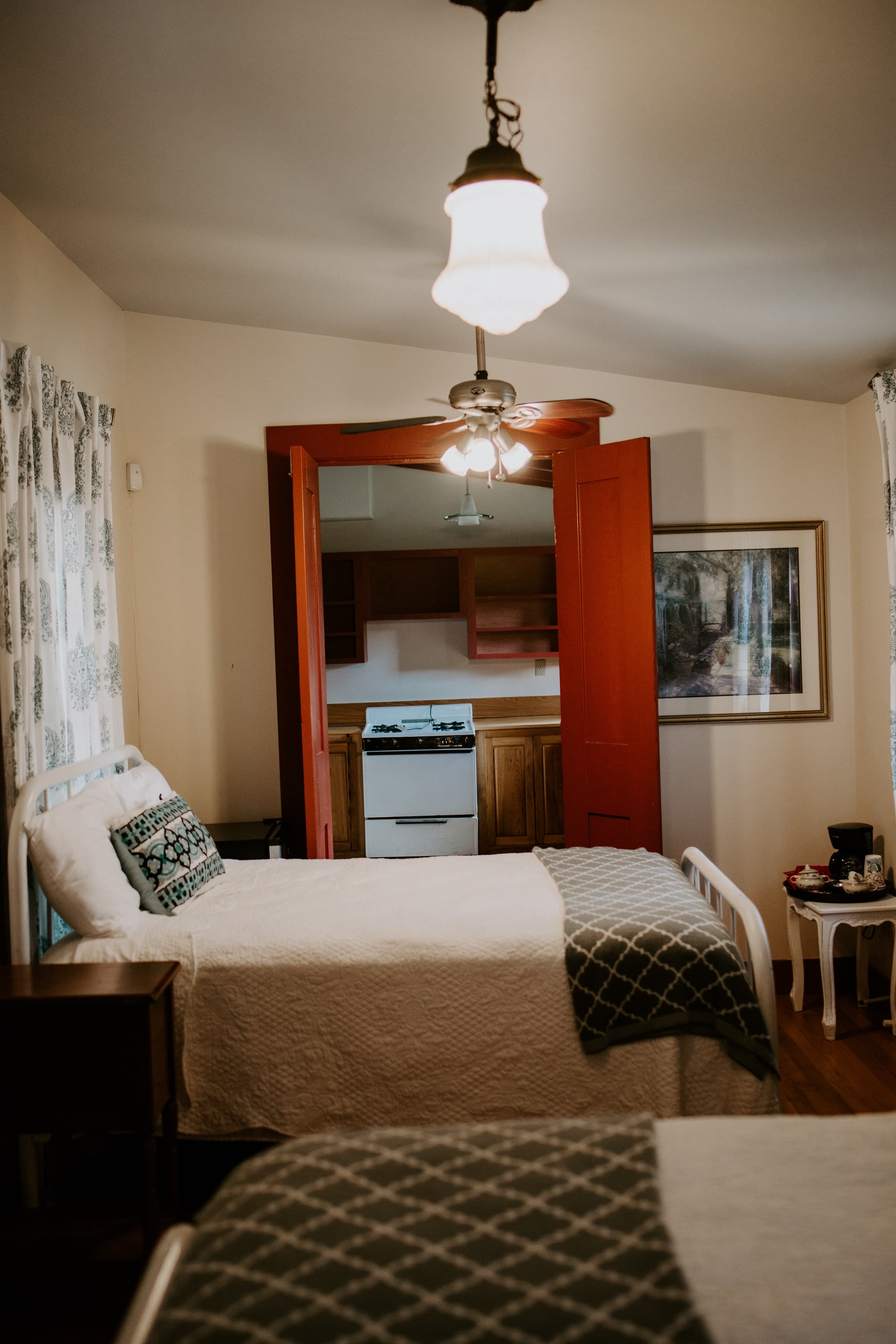 A cozy bedroom with two beds, a ceiling fan, and a doorway leading to a small kitchen area.