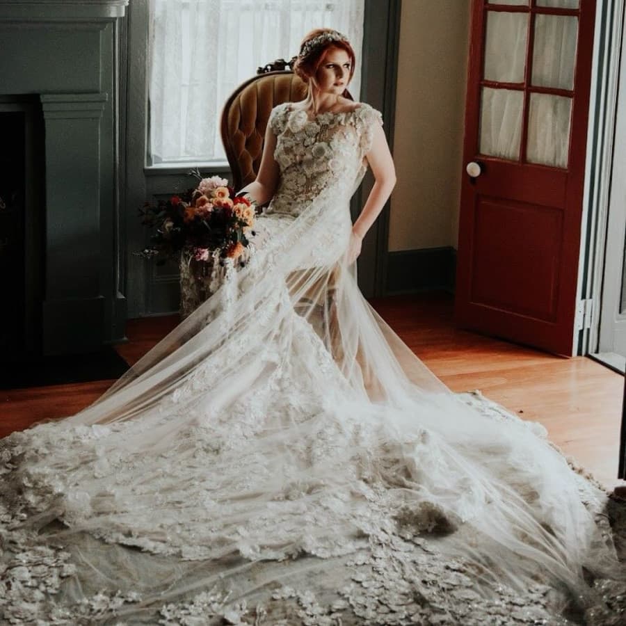 A bride in a stunning lace wedding gown poses gracefully in a vintage room.