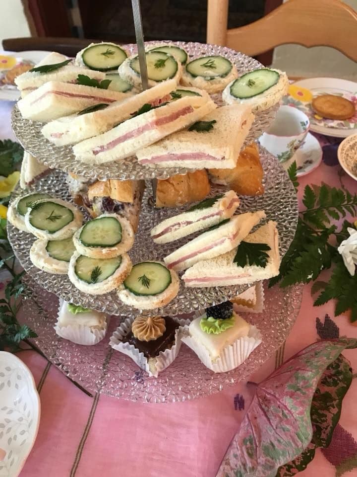 A tiered serving platter displays an assortment of cucumber sandwiches and small pastries.