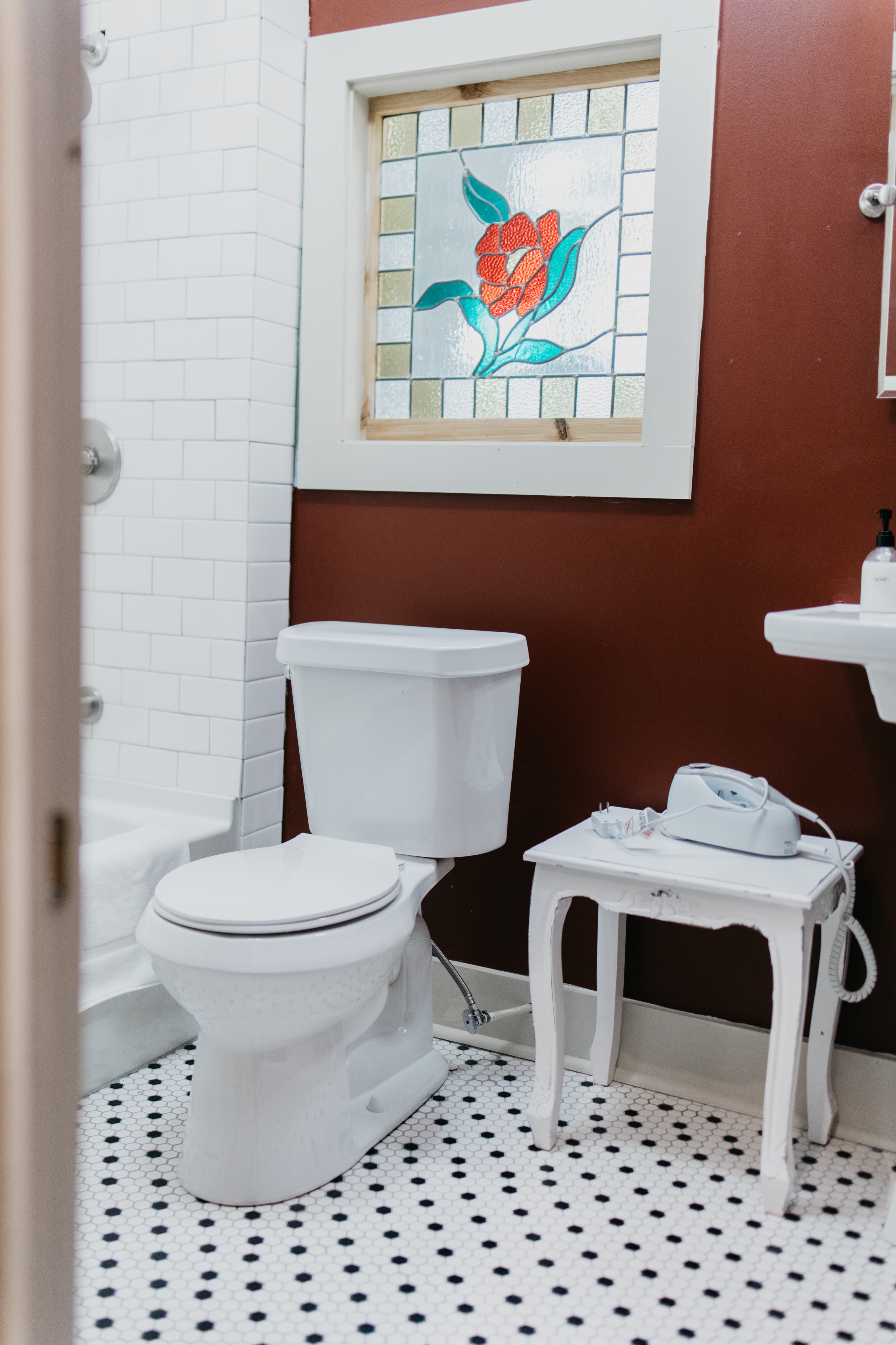A compact bathroom featuring a toilet, a decorative stained glass window, and a small table with a phone.