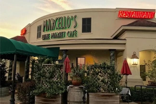Exterior of Marcello's Wine Market Café featuring a green awning and red umbrellas.