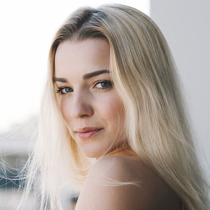 A young woman with long blonde hair gazes over her shoulder, showcasing a serene expression.