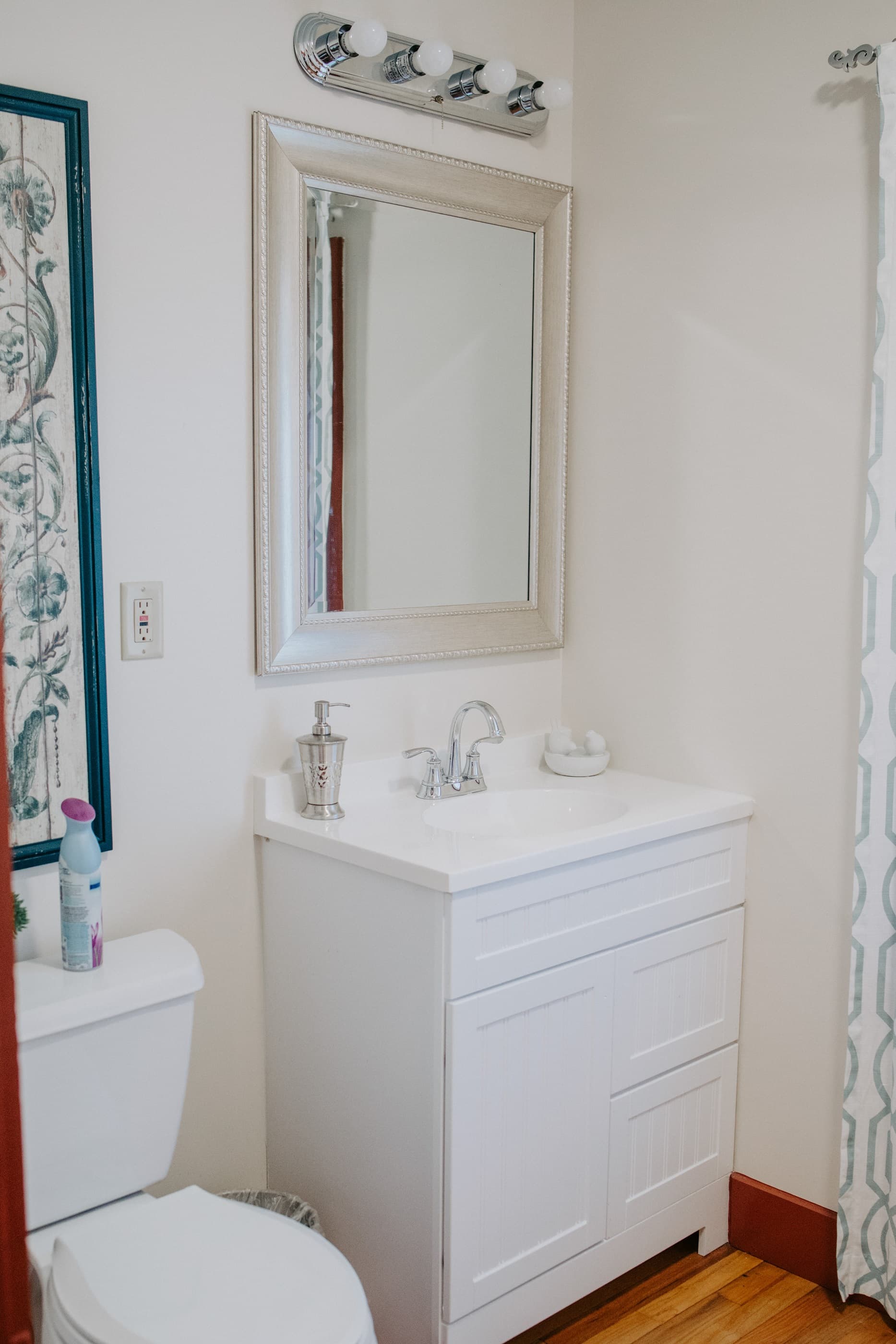 A modern bathroom featuring a white vanity, mirror, and a toilet beside a window.