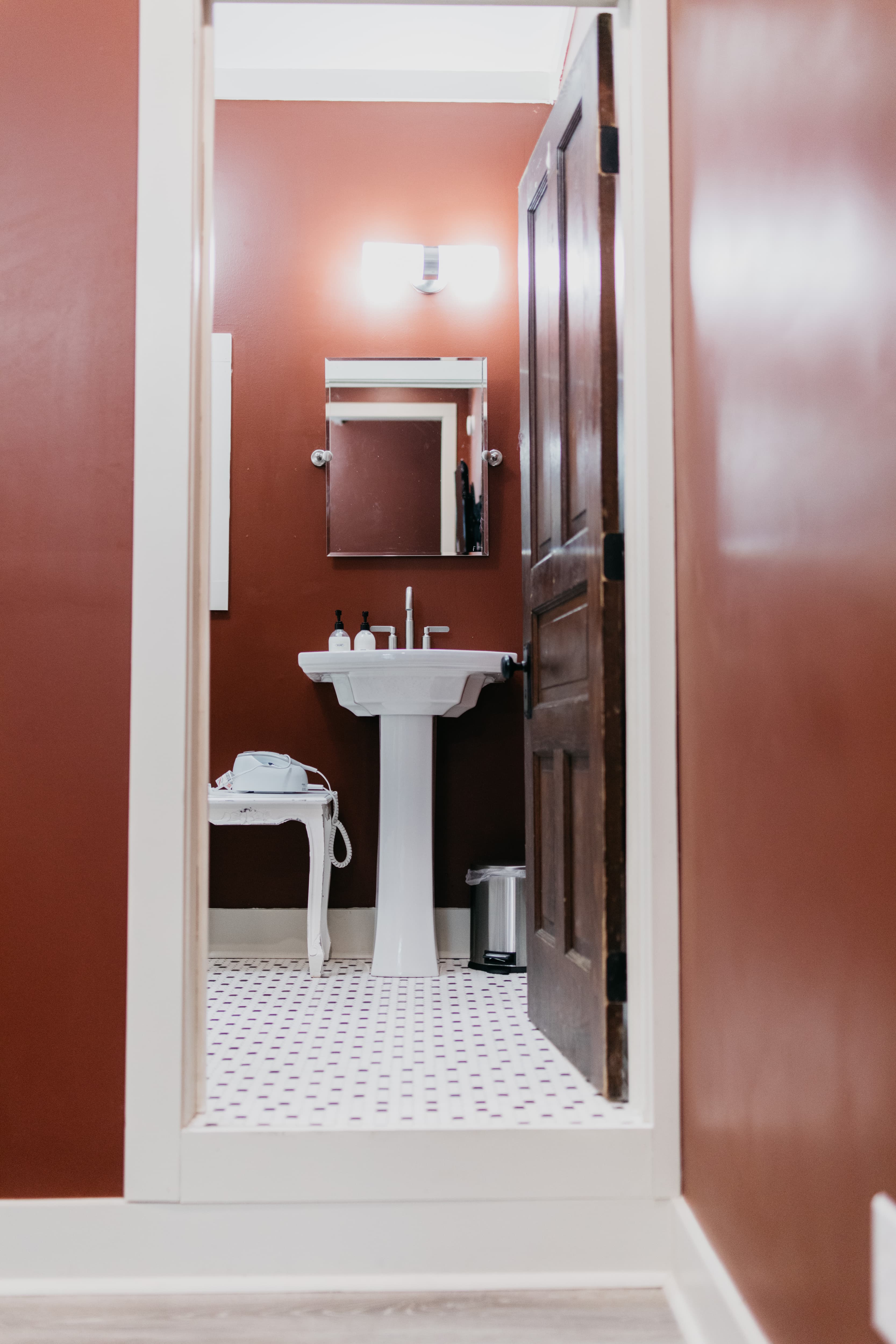 View of a small bathroom with a sink, mirror, and vintage decor, framed by a doorway.