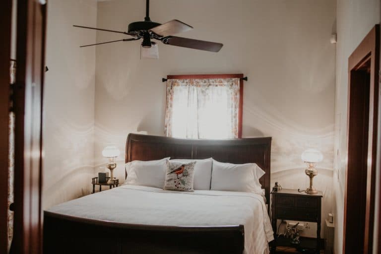 A cozy bedroom featuring a large bed with white linens, a ceiling fan, and two lamps beside the nightstands.