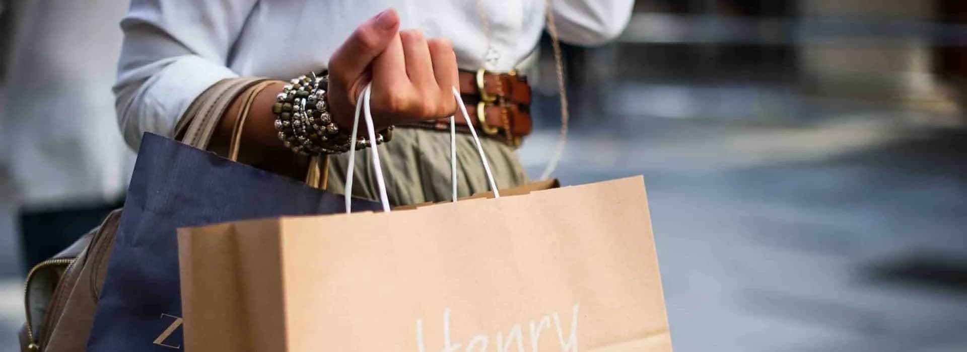 A person holds several shopping bags while wearing a stylish outfit and accessories.