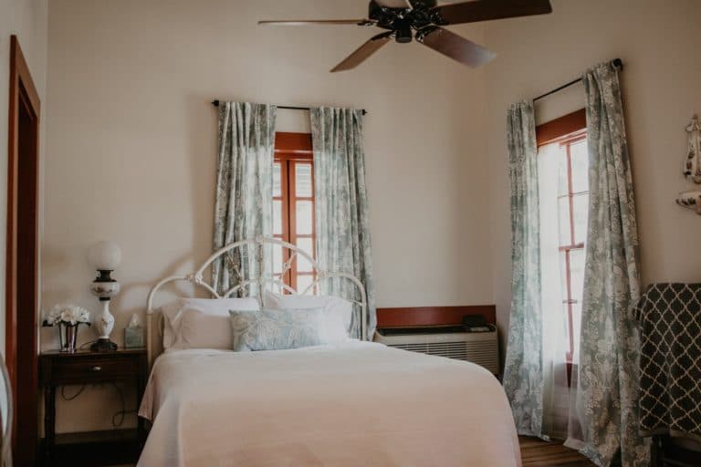 A cozy bedroom featuring a white bed, floral curtains, and a ceiling fan.