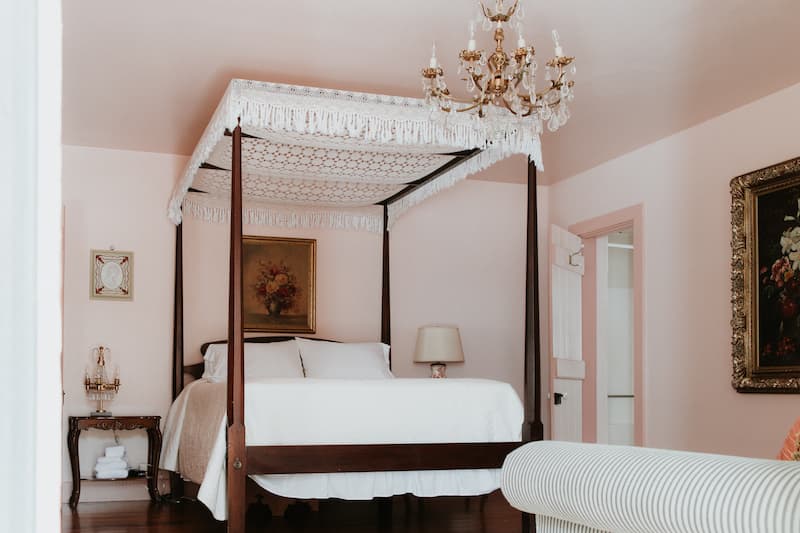 A cozy bedroom featuring a four-poster bed, chandelier, and pastel walls.