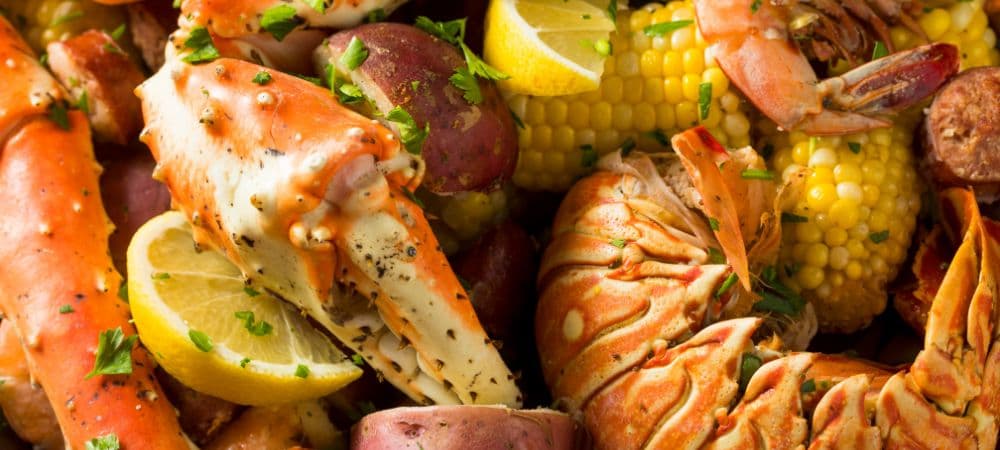 A vibrant seafood platter featuring crab legs, lobster, shrimp, potatoes, corn, and lemon wedges.
