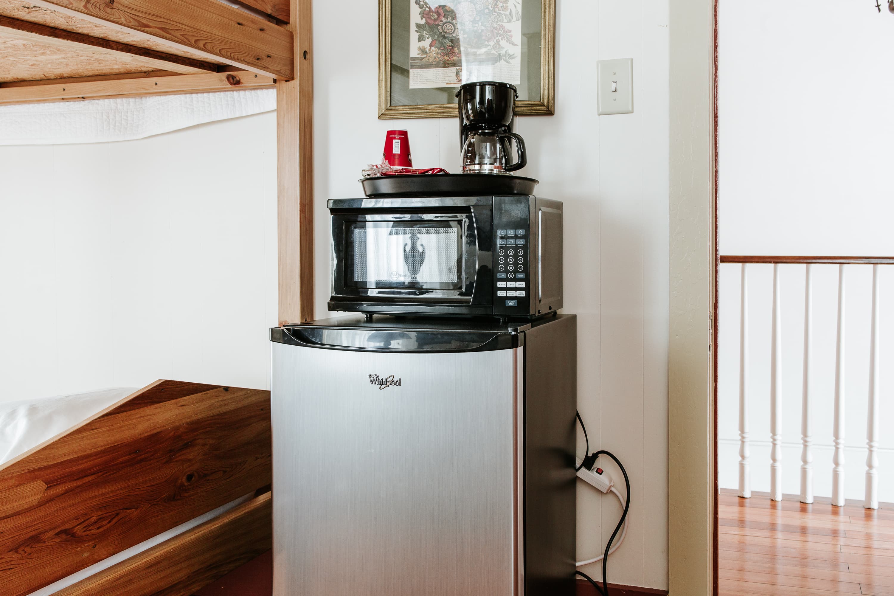 A small kitchen setup featuring a microwave and coffee maker atop a mini refrigerator in a cozy room.