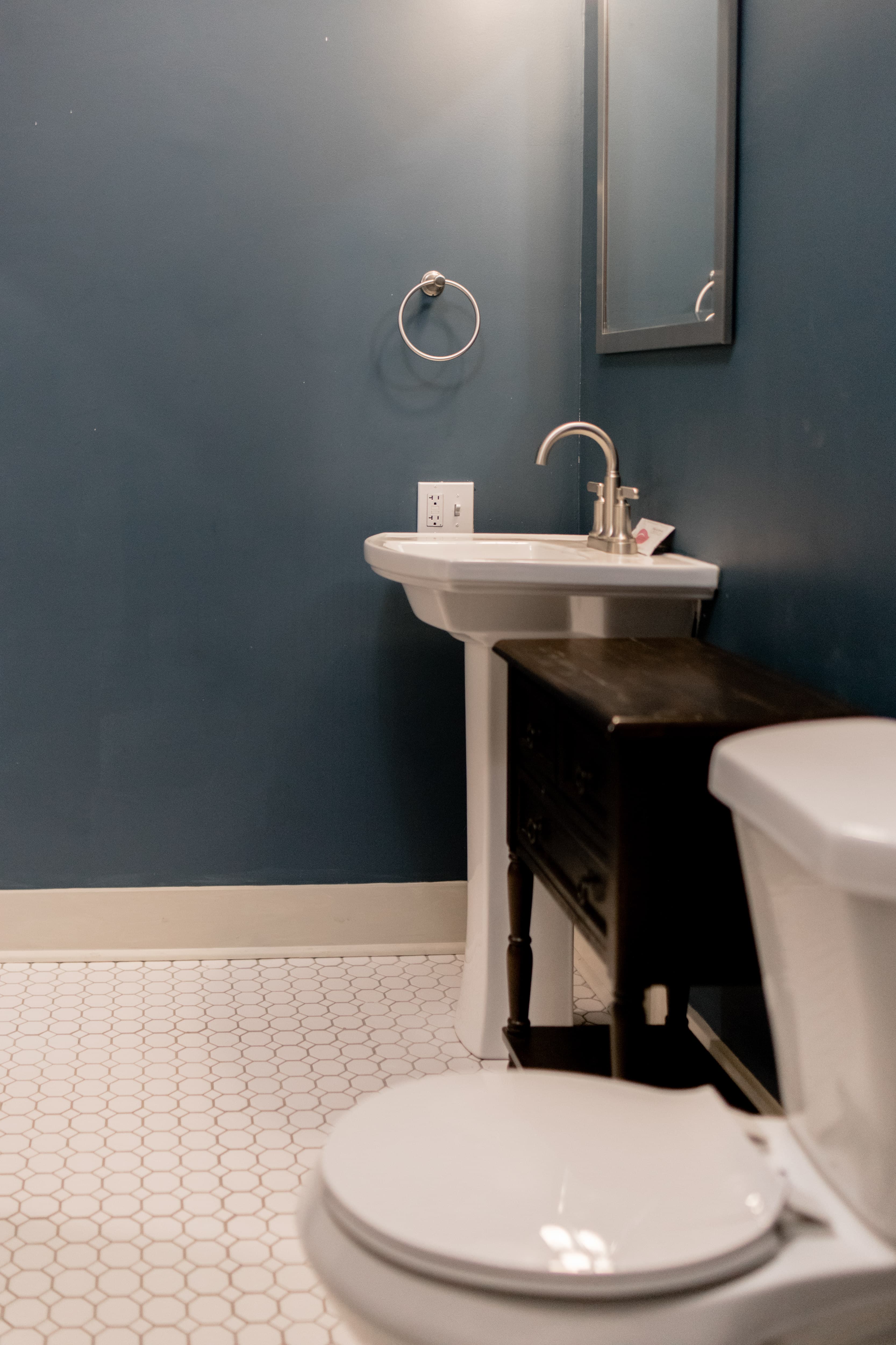 A small bathroom featuring a white sink, a toilet, a mirror, and dark blue walls.