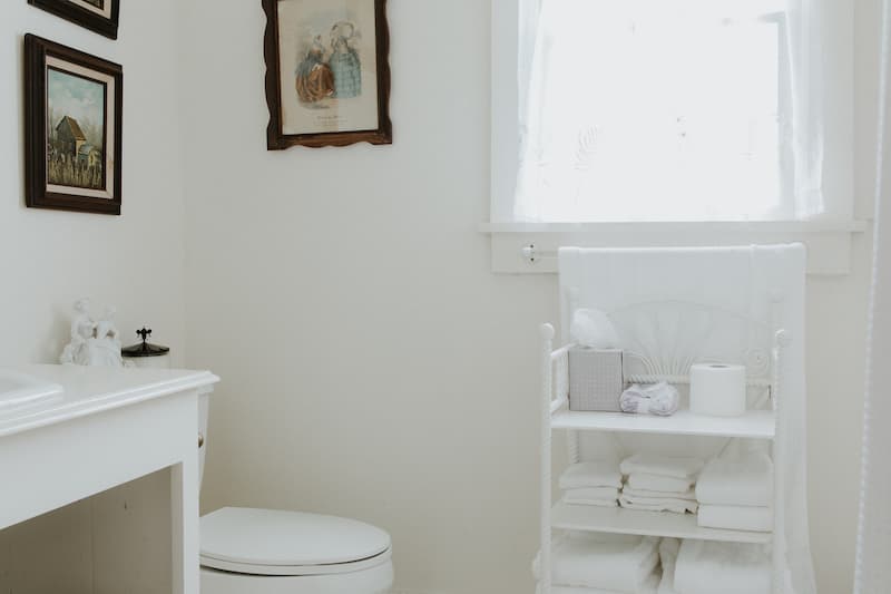 A bright, clean bathroom featuring a white toilet, neatly folded towels, and framed artwork on the walls.