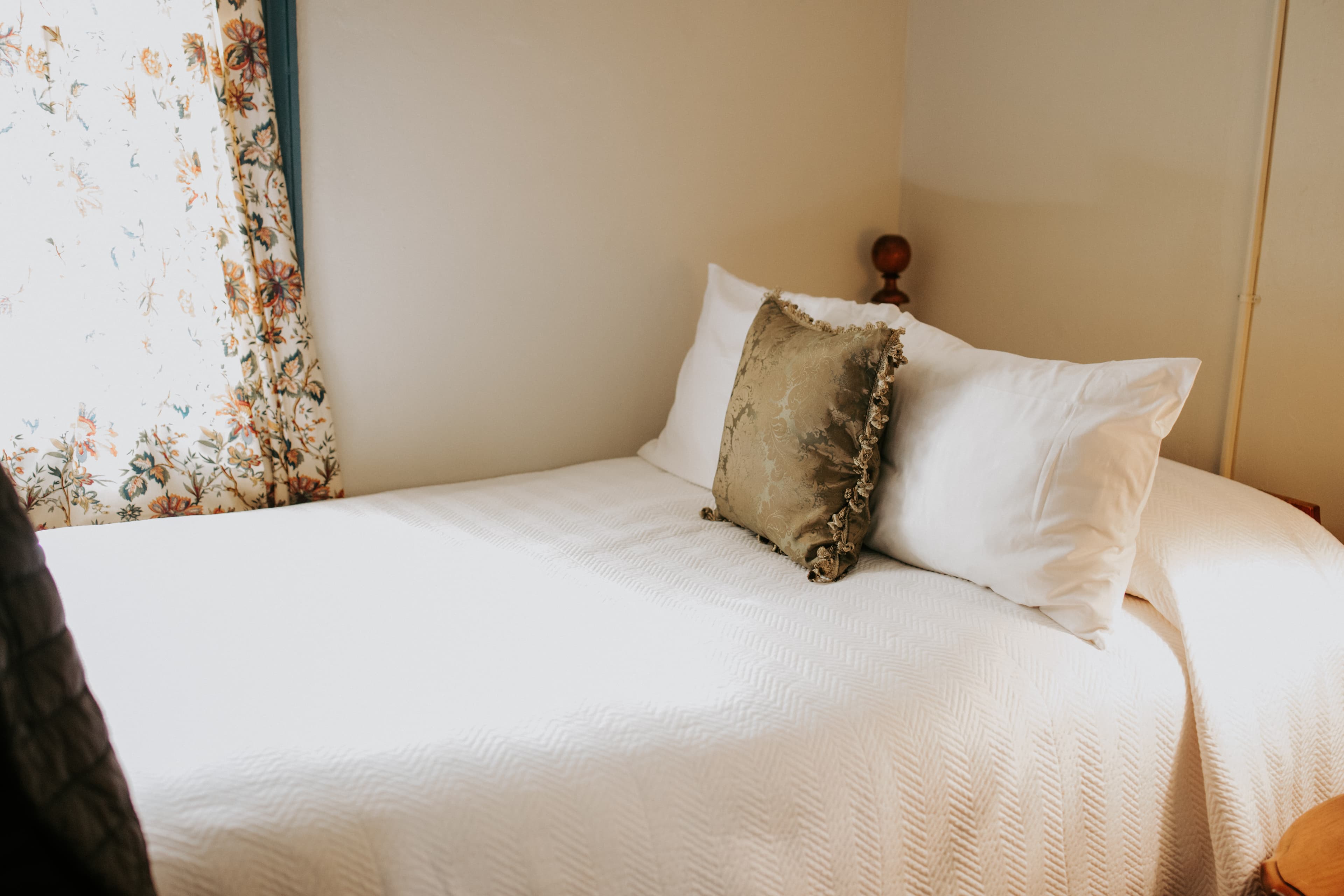 A neatly made bed with decorative pillows beneath a window with floral curtains.
